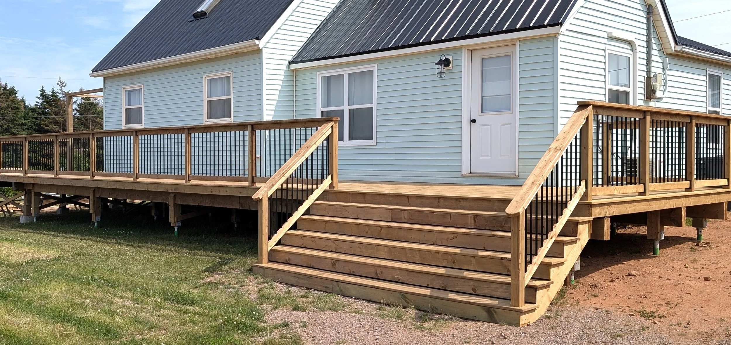 Custom design and built, pressure treated wooden deck with wide stairs and black aluminum railing built for homeowner in Wild Harbour, PEI