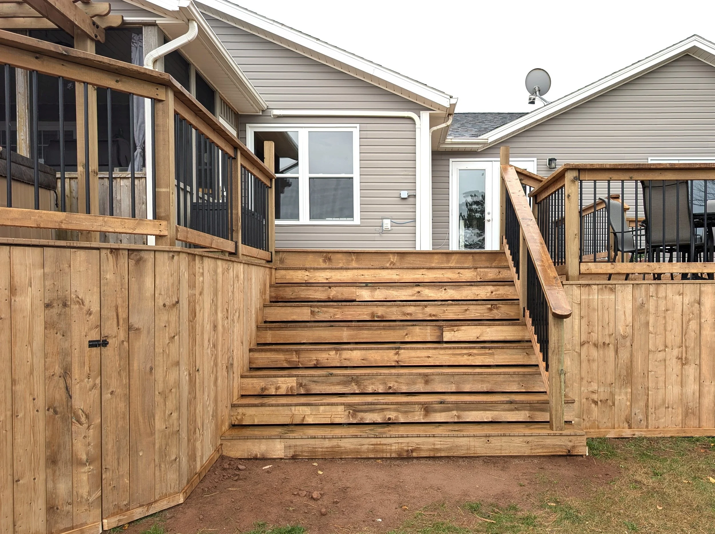 Custom design and built, pressure treated, multi level wooden deck with inset wide stairs and black aluminum railing built for homeowner in West Covehead, PEI