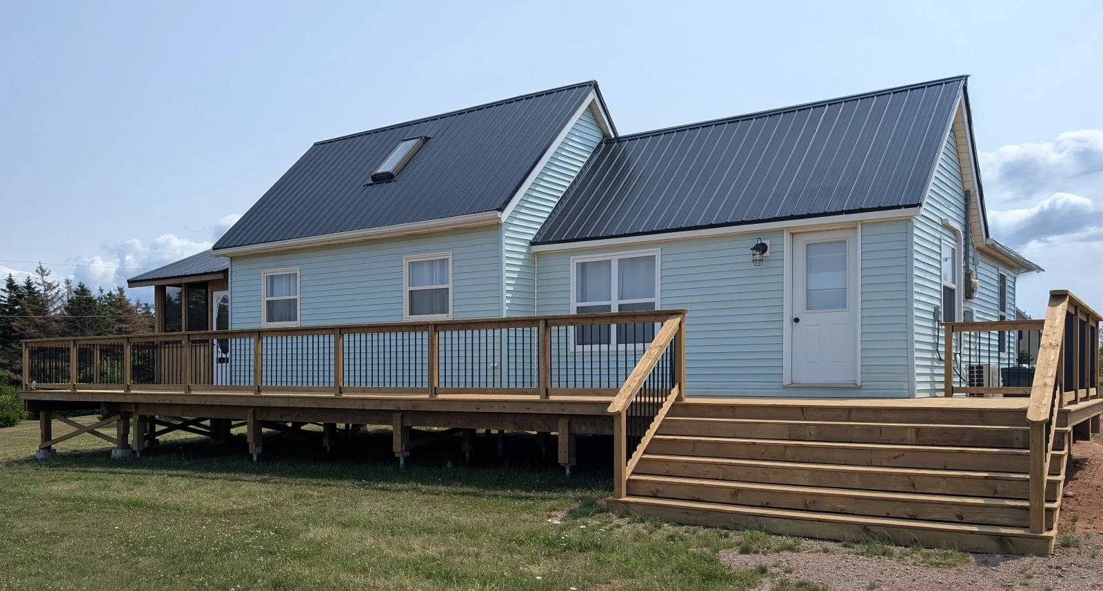 Custom designed, wrap around, pressure treated, wooden deck with screen enclosed pergola, 12 ft wide stairs and black aluminum railings built for a home owner in Wild Harbour, PEI