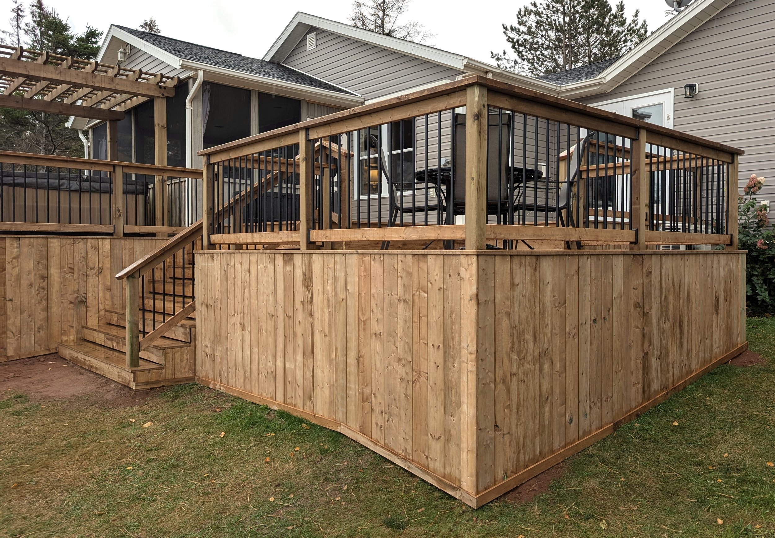 Custom design pressure treated wood pergola on multi-level deck with black aluminum railings and stairs built for a homeowner in West Covehead, PEI 