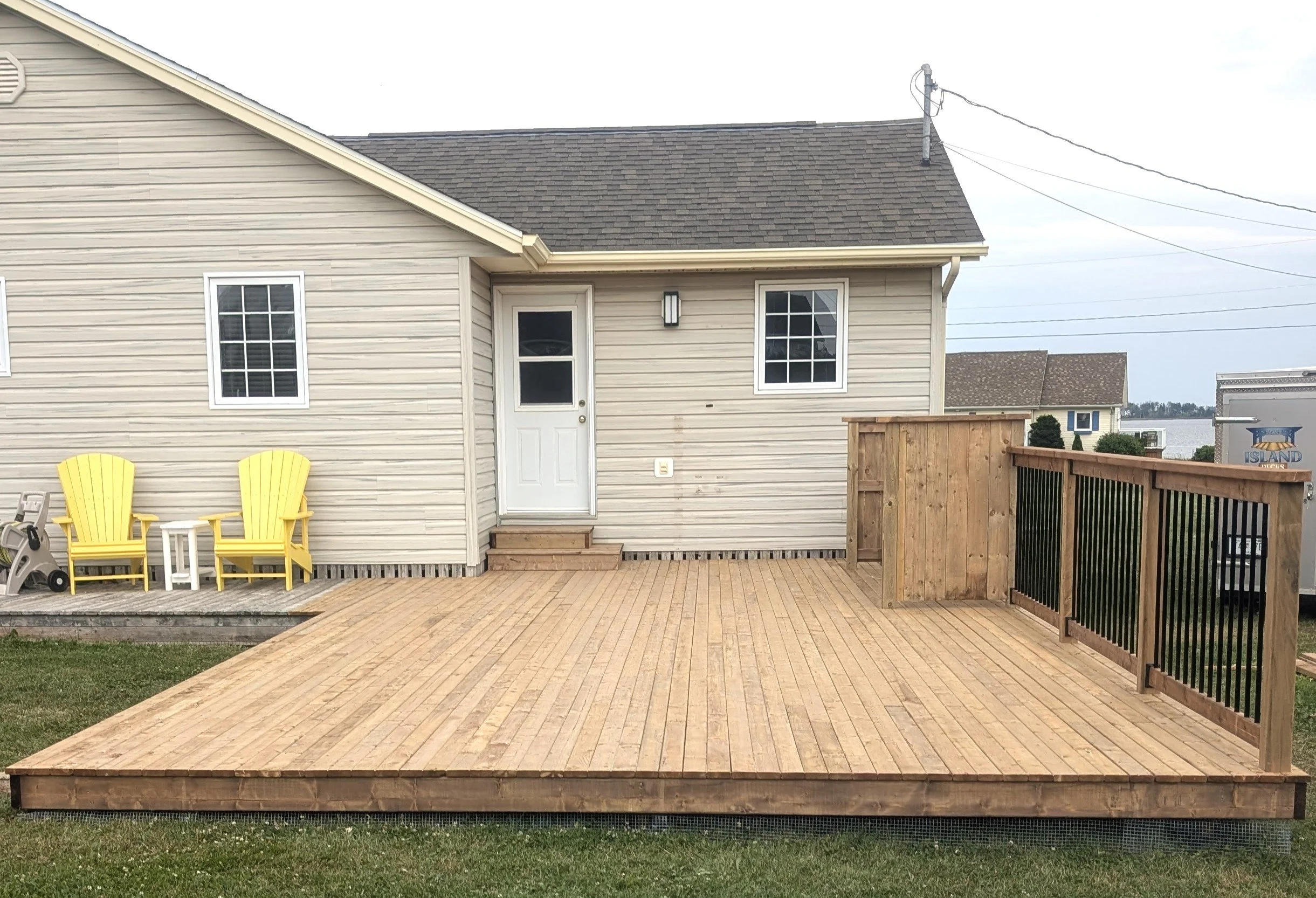 Custom built, pressure treated, ground level wooden deck with black aluminum railings and BBQ corral, built for a cottage owner in Stanley Bridge, PEI