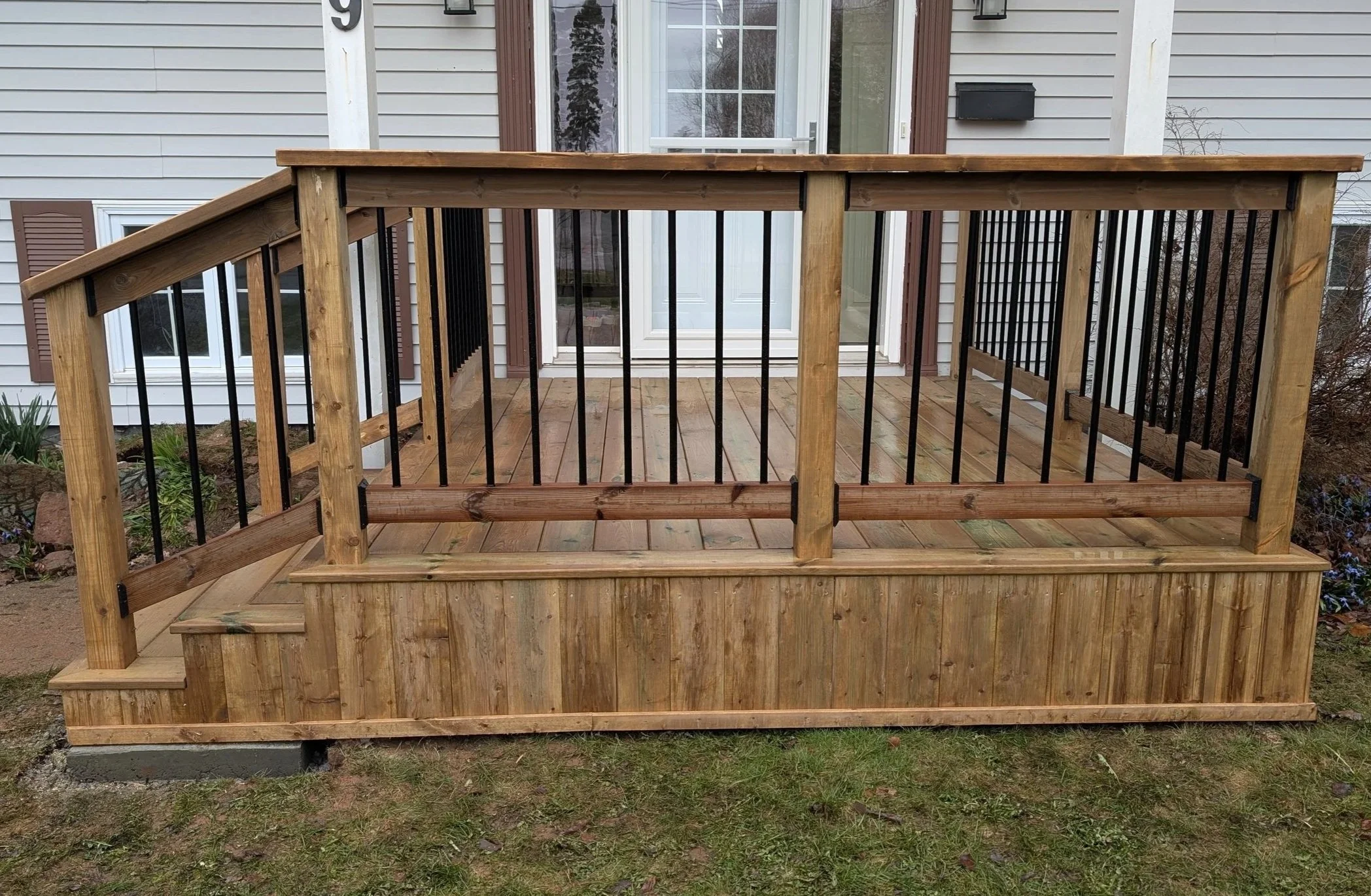 Completed pressure-treated wooden front deck and door step with black aluminum railings, Charlottetown, Prince Edward Island