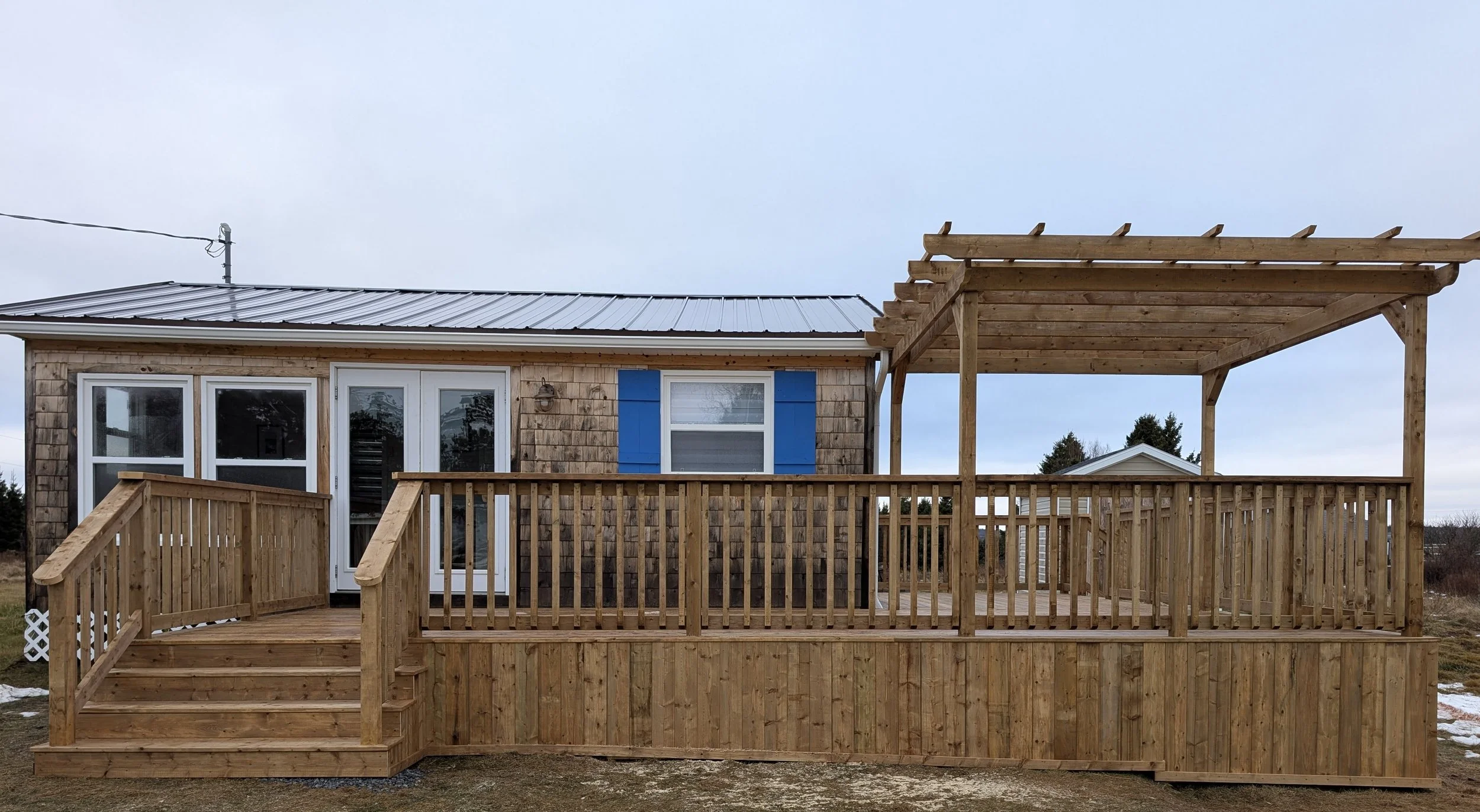 Custom pressure treated wooden deck with wood pergola and railings built for a cottage owner in Canoe Cove, PEI