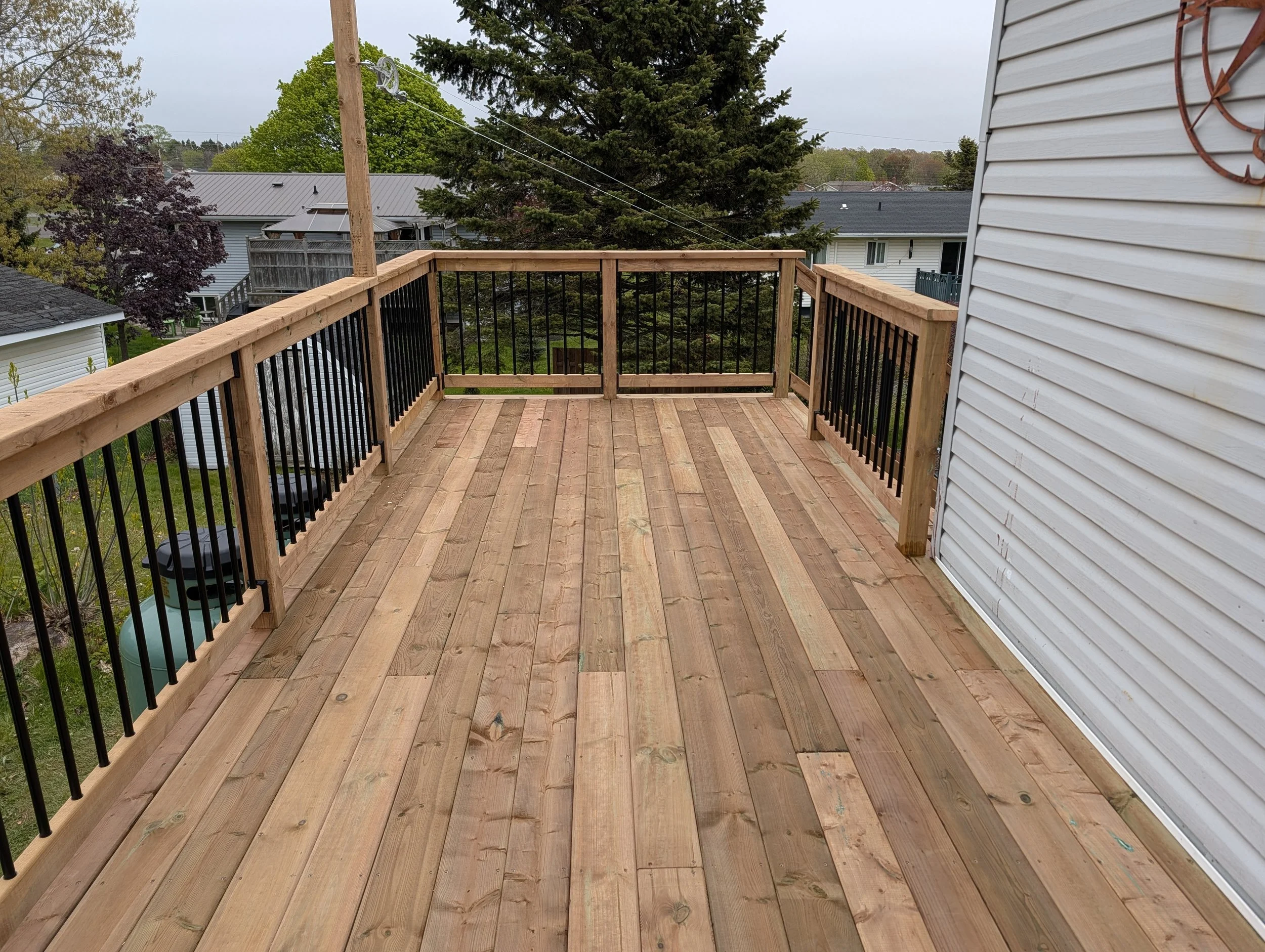 Custom pressure-treated upper and lower wood deck and connecting stairs with black aluminum railings built in Charlottetown, Prince Edward Island.