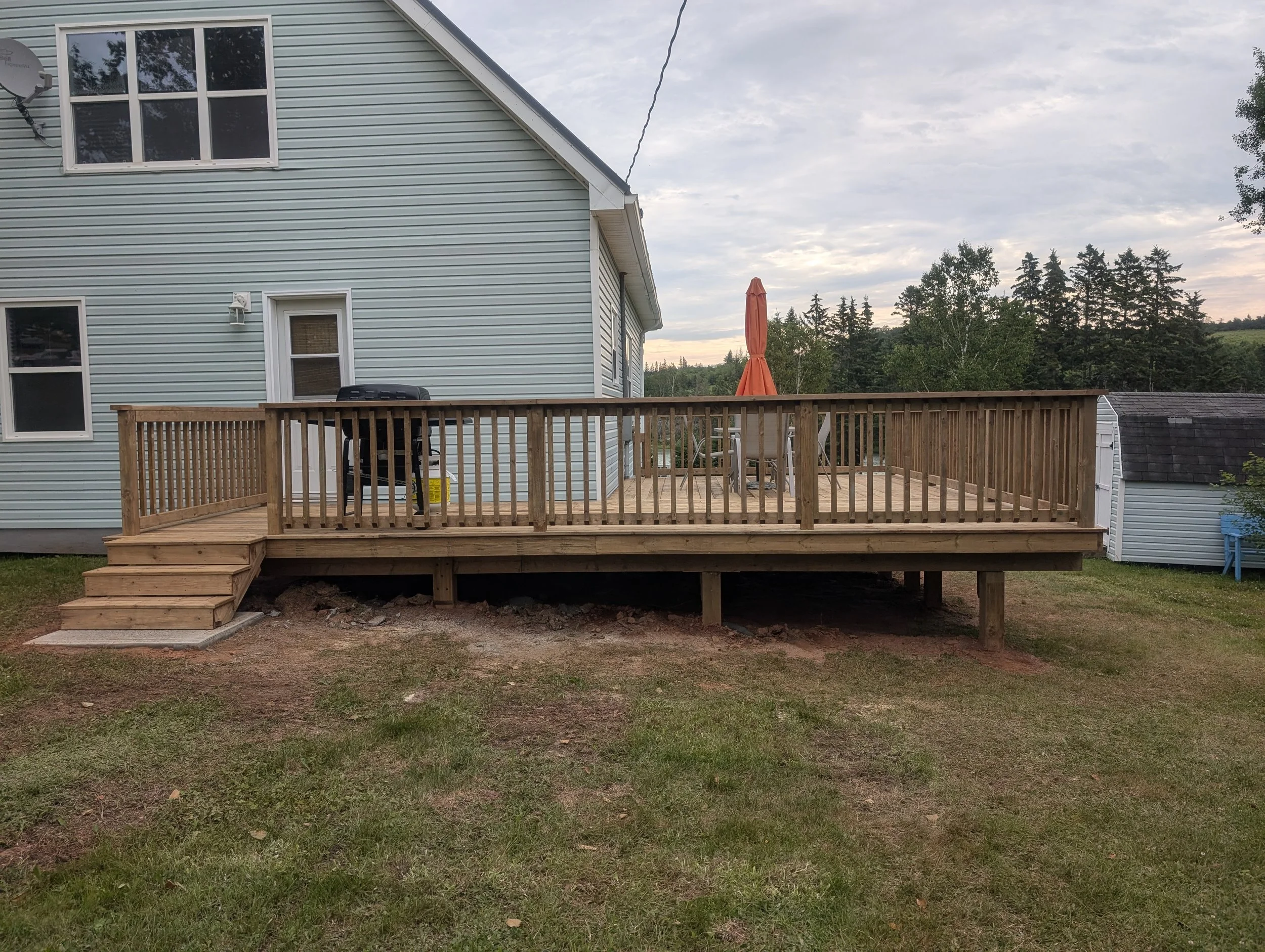 Custom built, pressure treated, wrap-around,  wooden deck with wood & black aluminum railings and stairs, built for a home owner in Wild Harbour, PEI