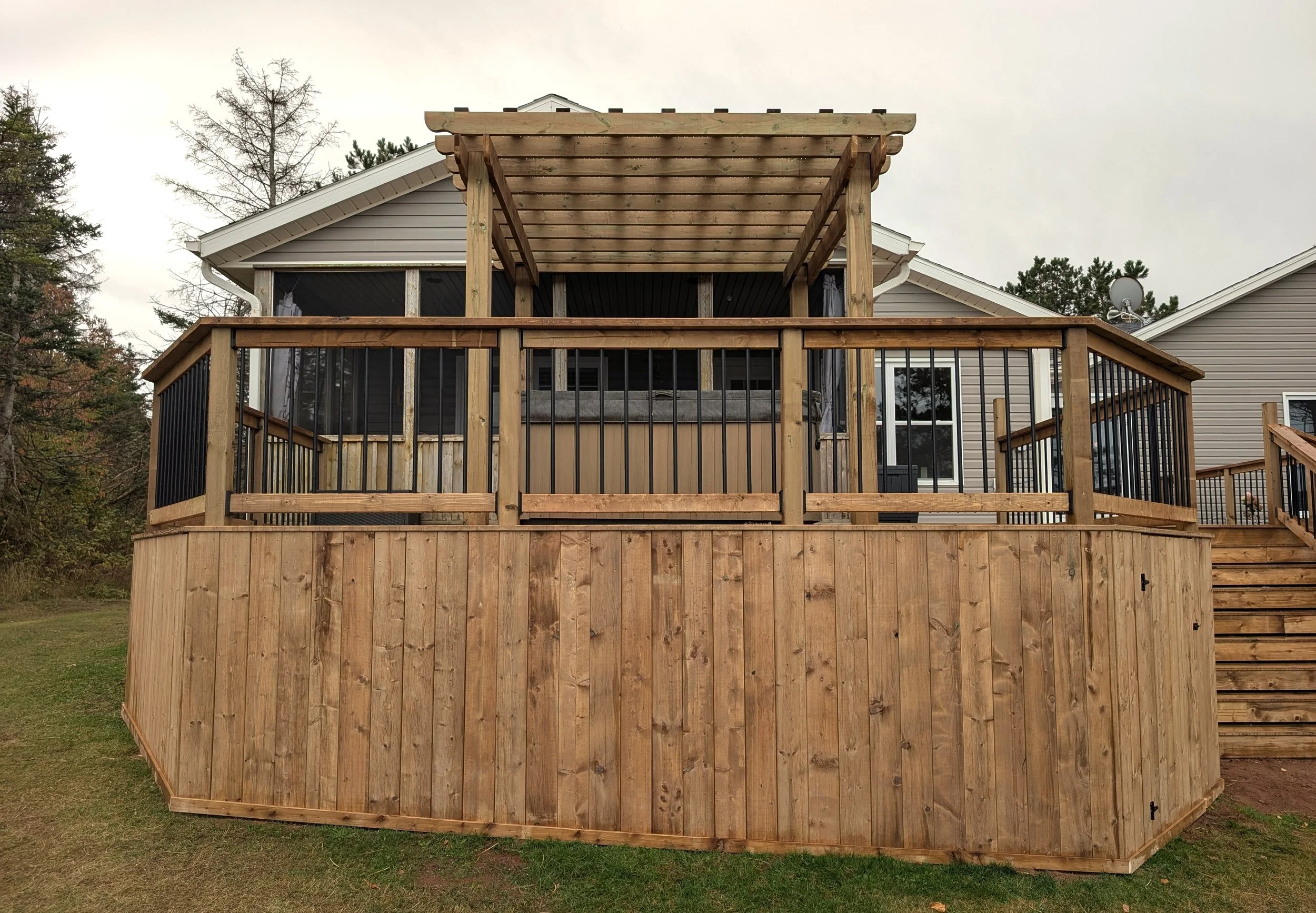 Custom design pressure treated wood pergola on multi-level deck with black aluminum railings and stairs built for a homeowner in West Covehead, PEI 
