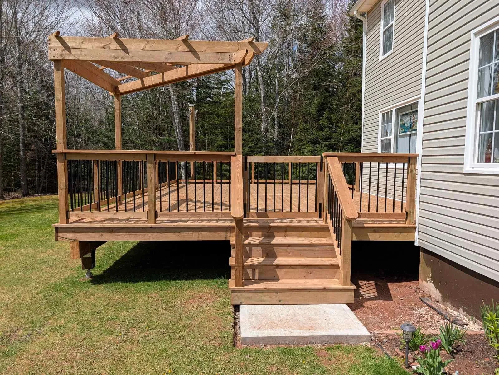 Custom design pressure treated corner wood pergola on deck with black aluminum railings and stairs built for a homeowner in Brackely Beach, PEI 