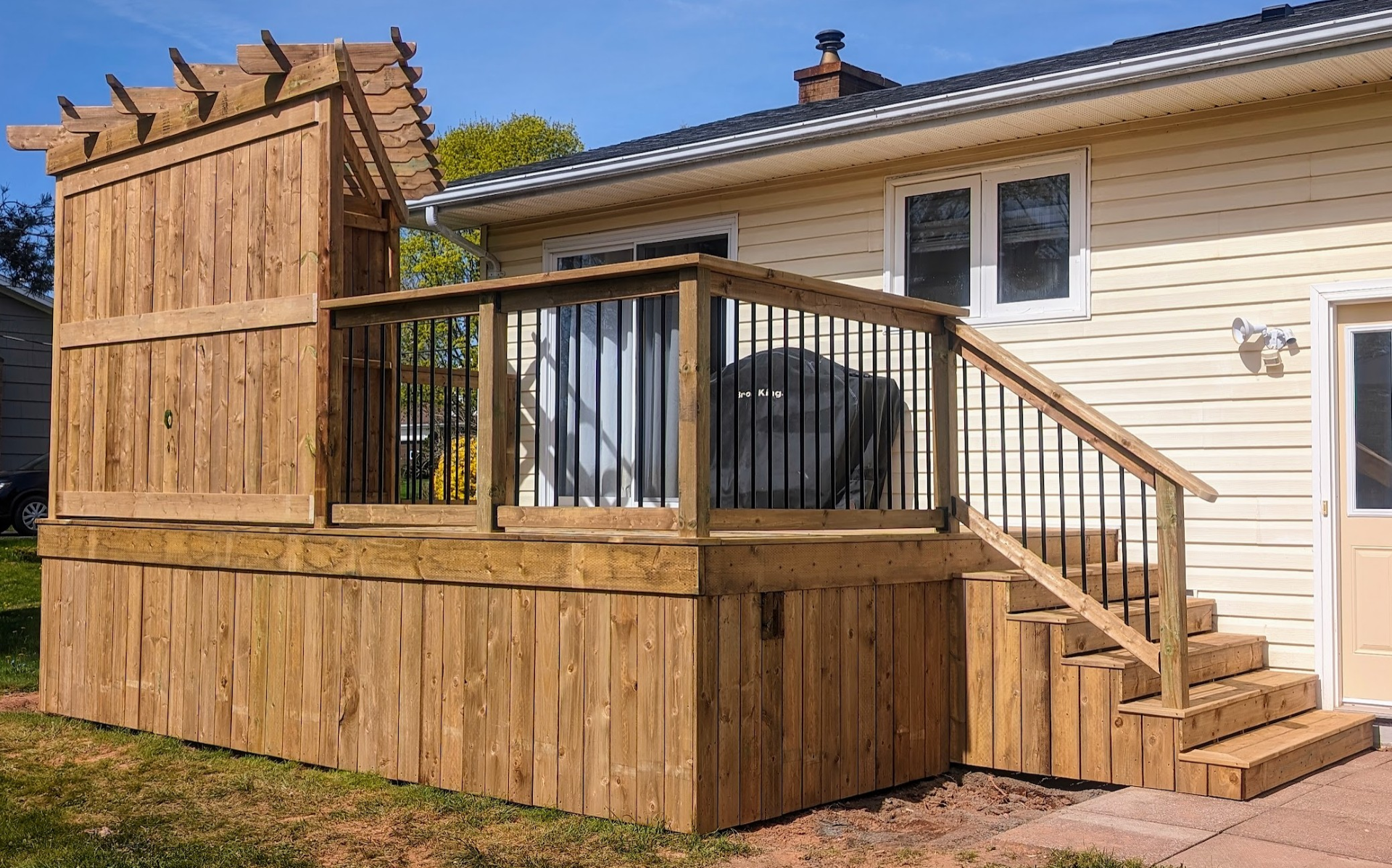 Custom built, pressure treated wooden deck with corner pergola, stairs, and black aluminum railings,  built for a home owner in Charlottetown, PEI