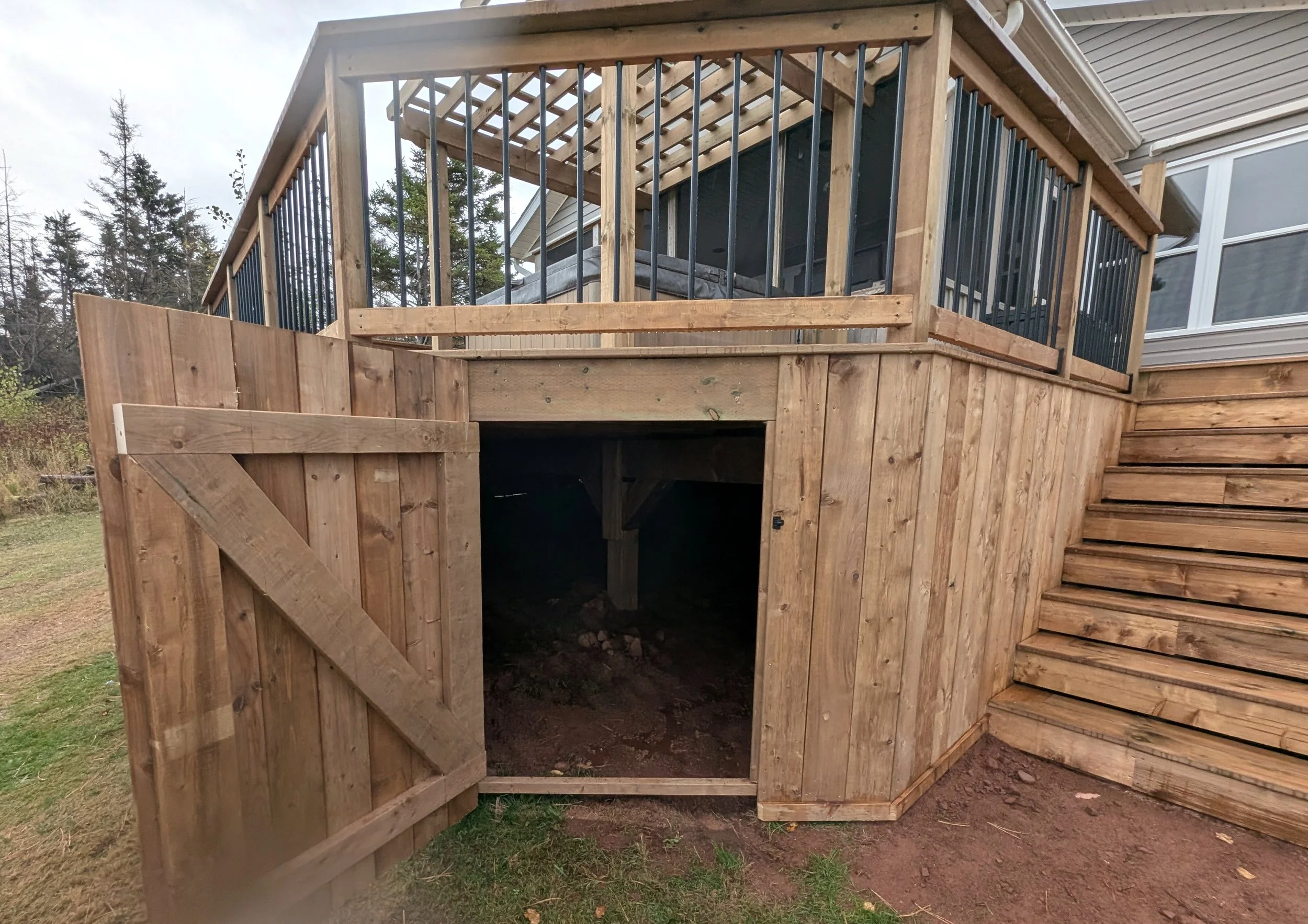 Custom design pressure treated wood pergola on multi-level deck with black aluminum railings, stairs and under deck storage built for a homeowner in West Covehead, PEI 