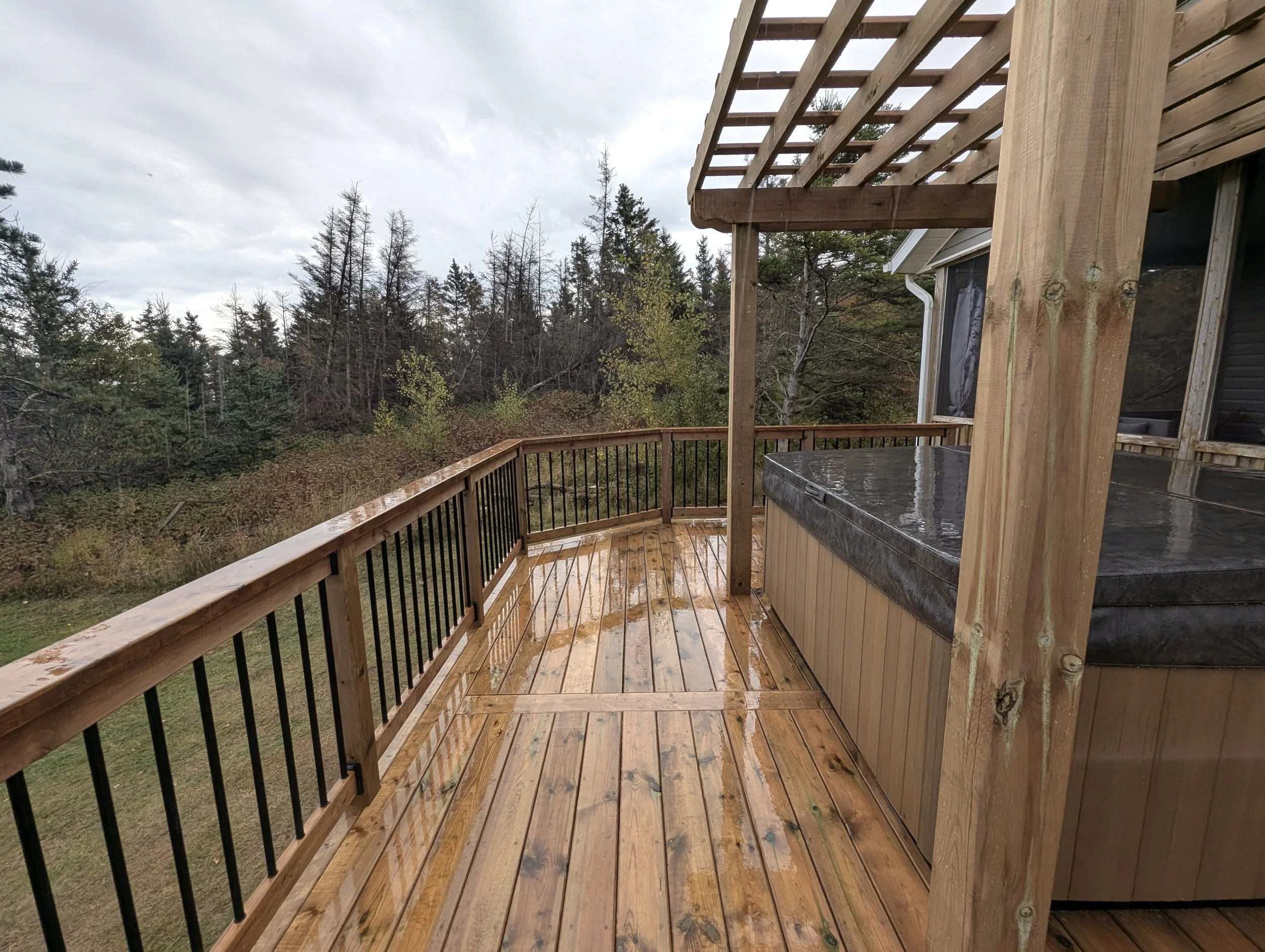 Custom design pressure treated wood pergola on multi-level deck with black aluminum railings and stairs built for a homeowner in West Covehead, PEI 
