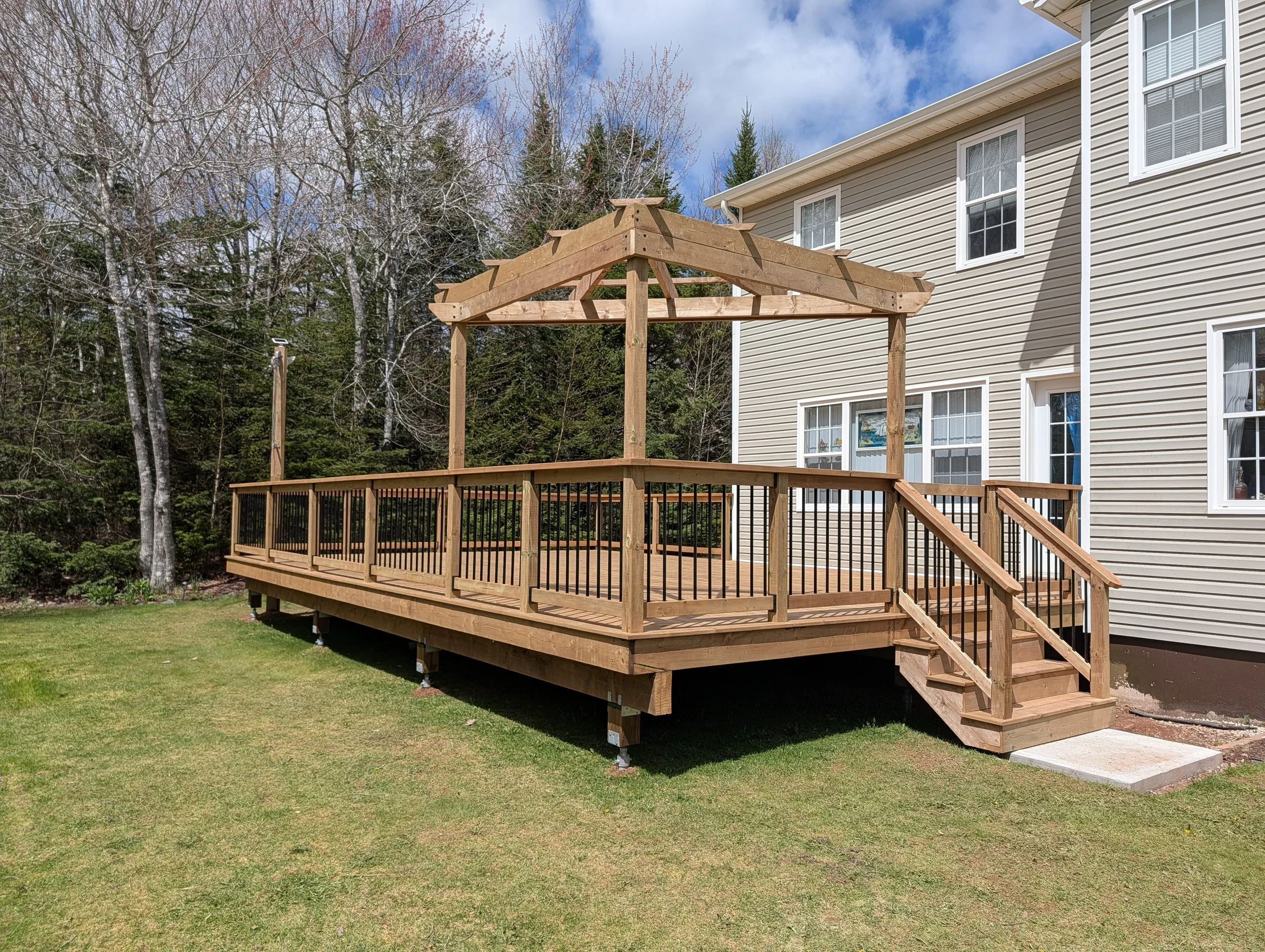 Completed pressure-treated wooden deck with pergola and black aluminum railings built in Brackley Beach, Prince Edward Island