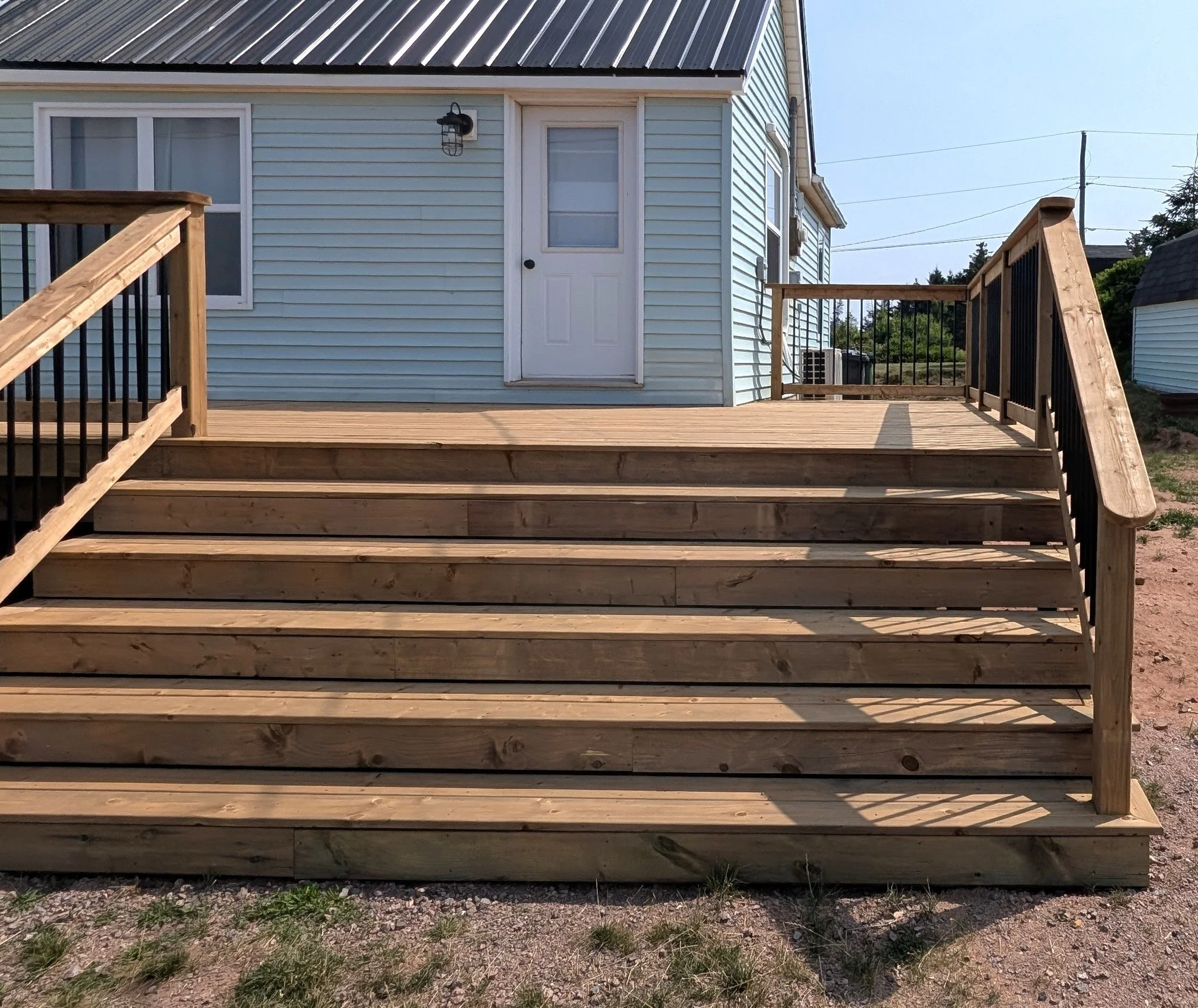 Custom design and built, pressure treated wooden deck with wide stairs and black aluminum railing built for homeowner in Wild Harbour, PEI