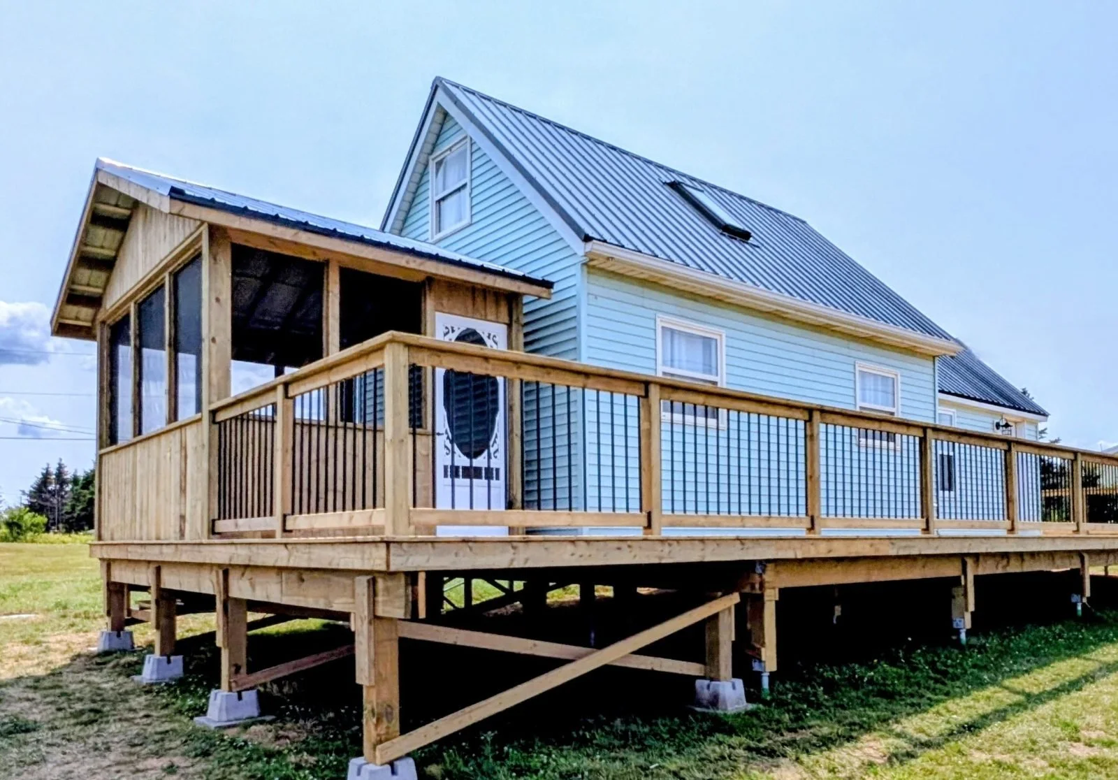 Custom built, pressure treated, wooden deck with a screened-in gazebo on wrap-around deck, and black aluminum railings,  built for a home owner in Wild Harbour, PEI 