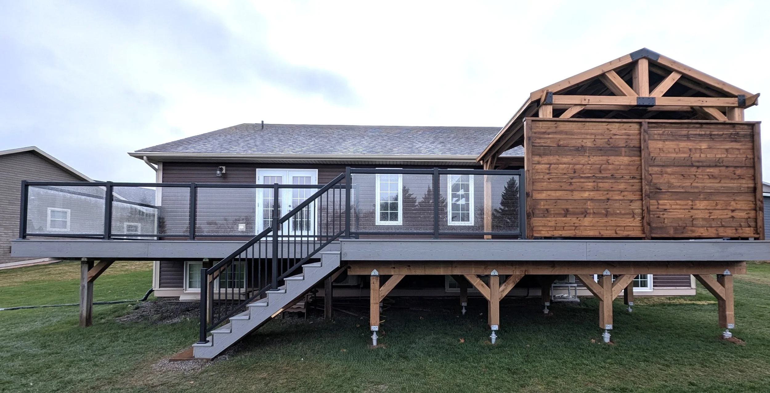 Custom pressure-treated wooden privacy wall on a composite deck with glass panels and aluminum railings built in Charlottetown, PEI