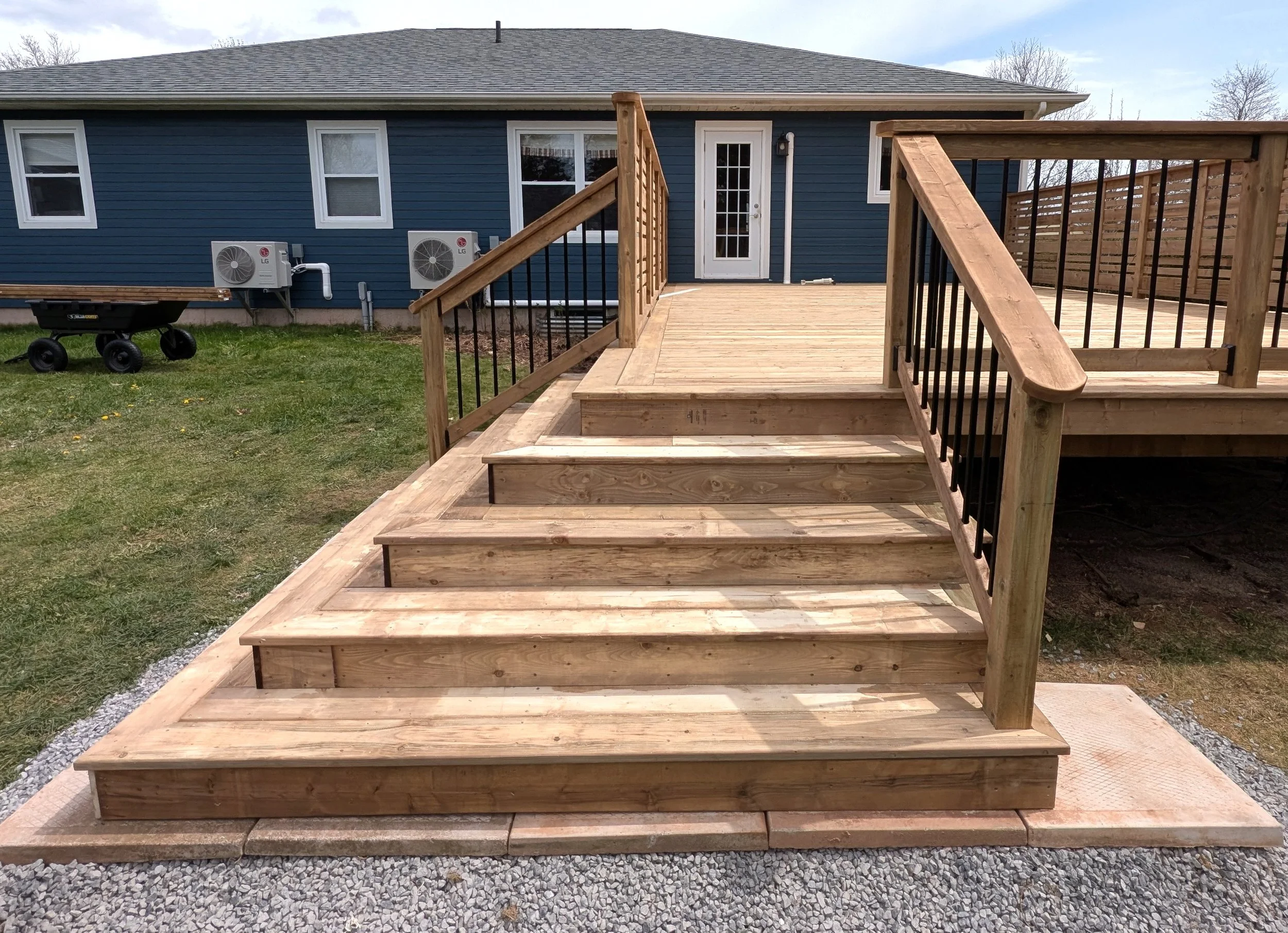 Custom design and built, pressure treated wooden deck with cascading stairs and black aluminum railing built for homeowner in Winsloe, PEI