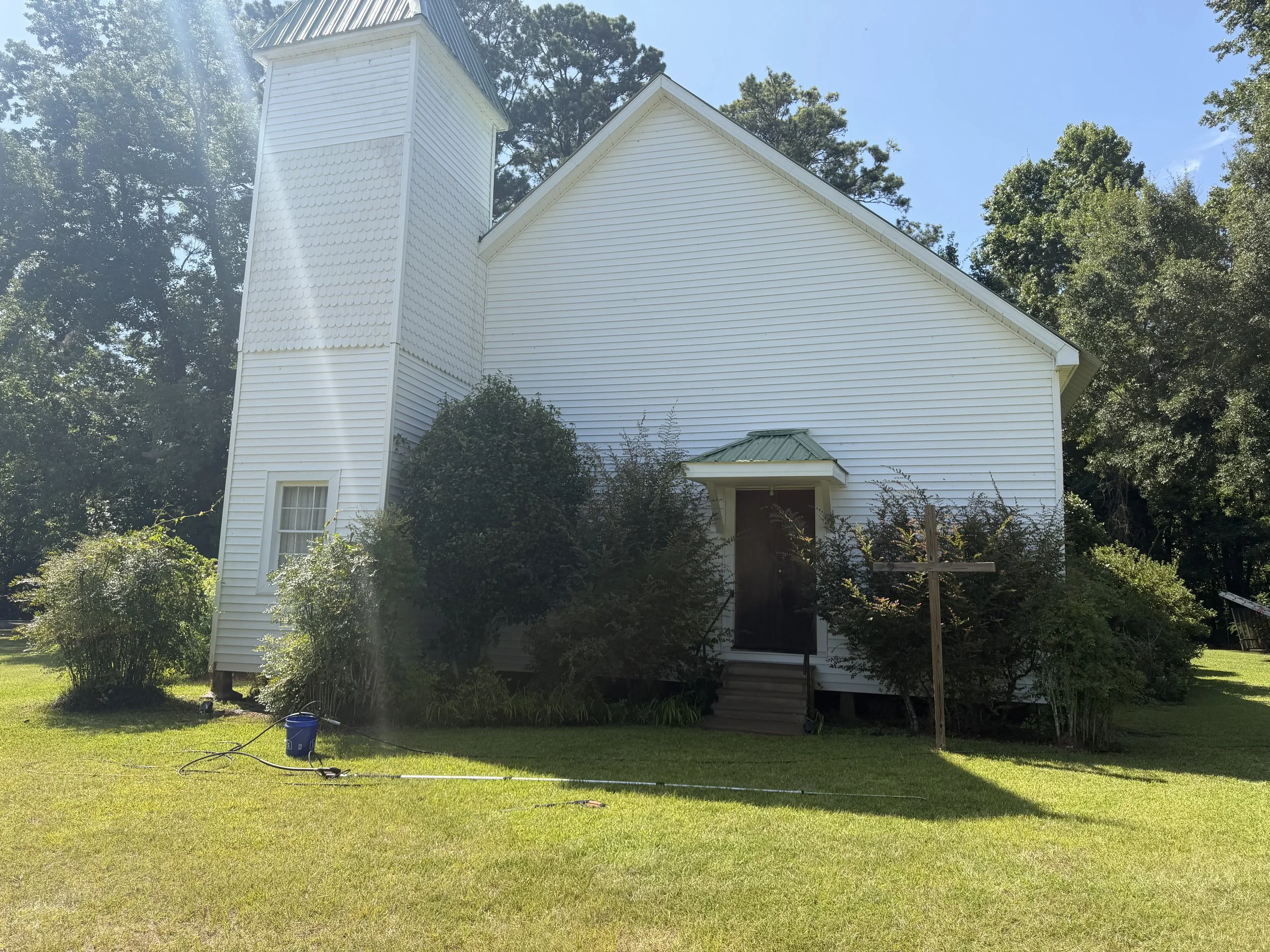 A white church with a steeple, surrounded by trees and a lawn, under a clear blue sky.
