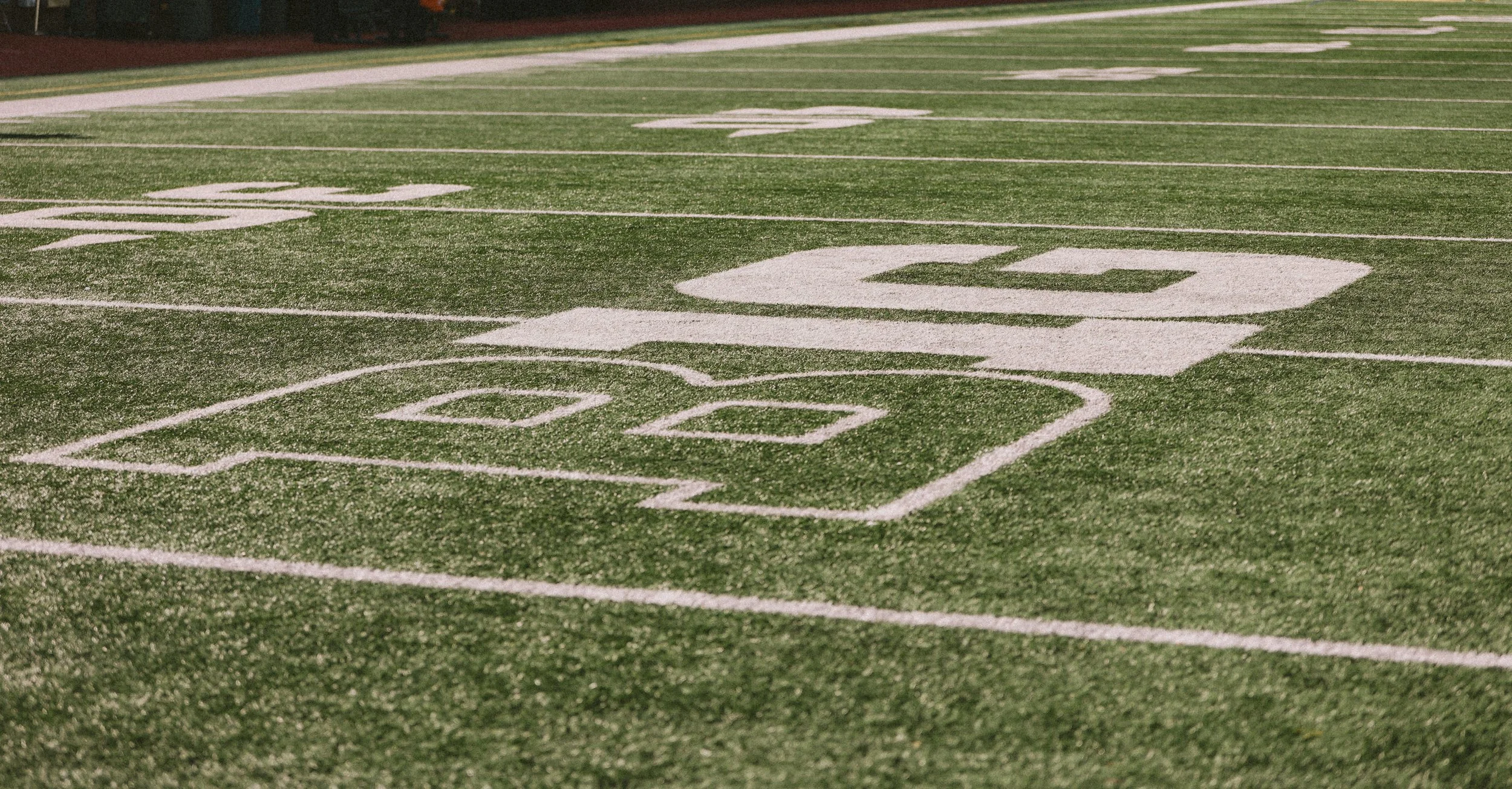Close-up of a football field with yard lines and numbers painted in white on artificial turf.