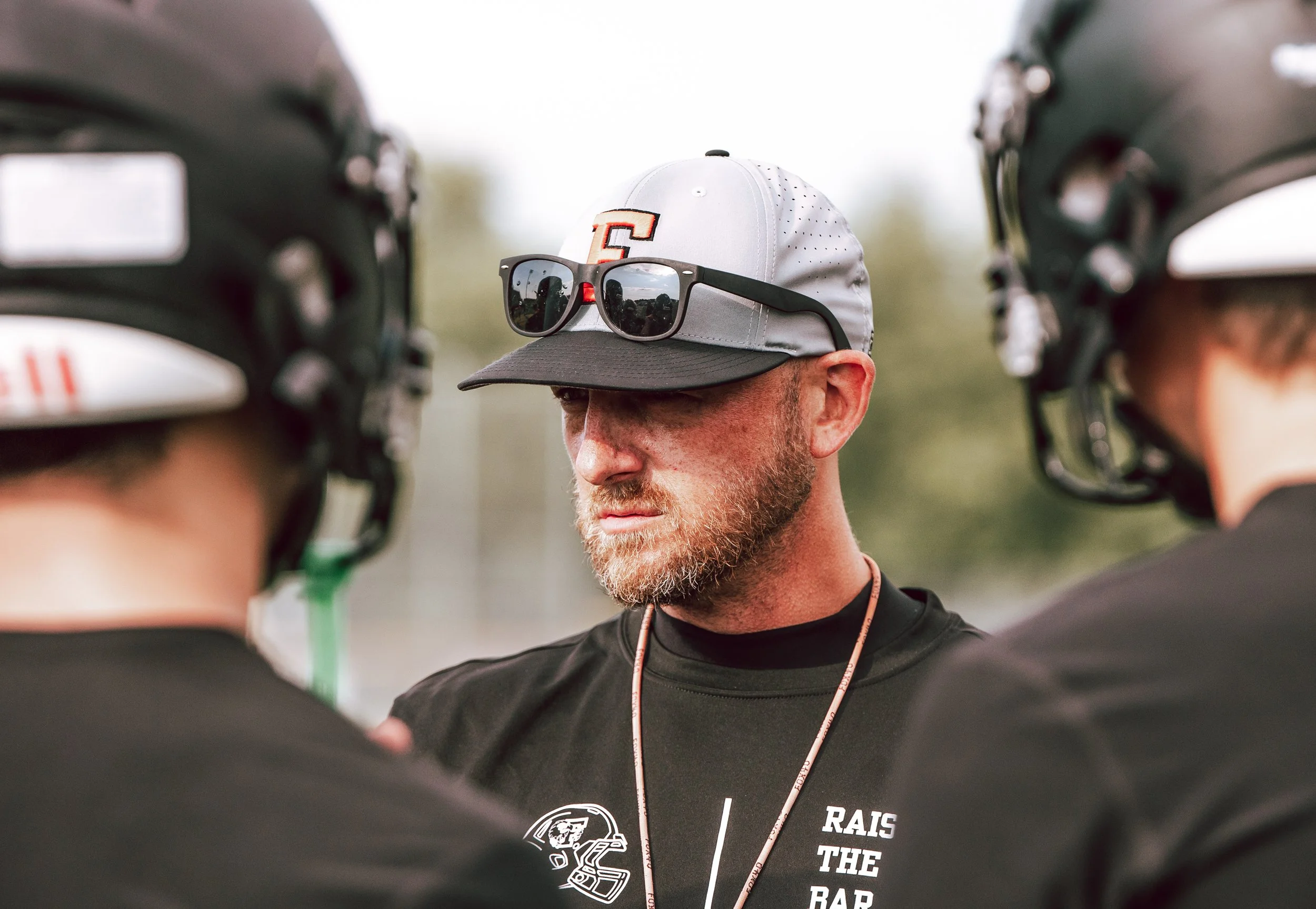 Three individuals with helmets, one with sunglasses and a cap, standing in a circle, possibly during a conversation or team meeting.