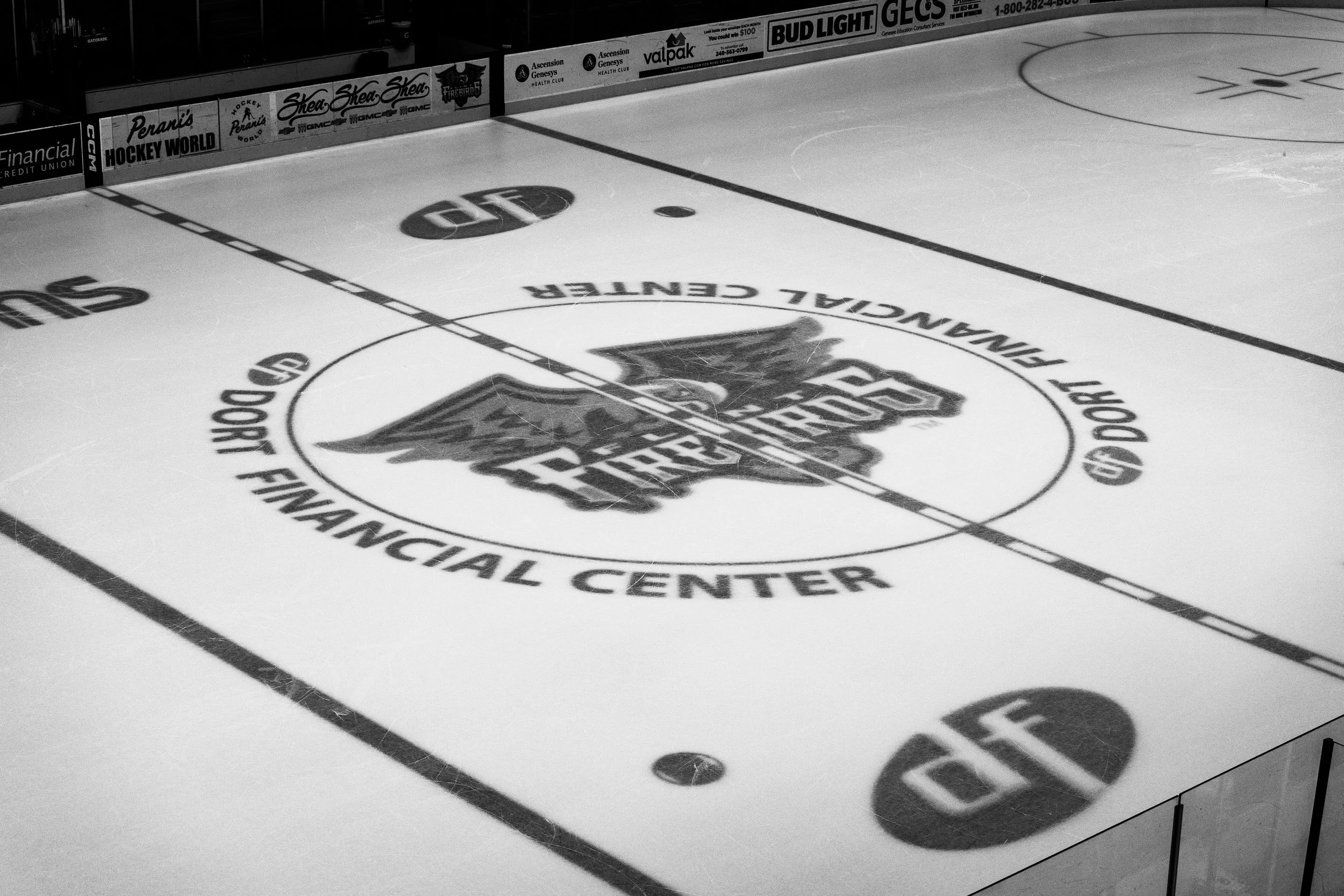 Black and white photo of an ice hockey rink with logos and advertisements on the ice and boards.