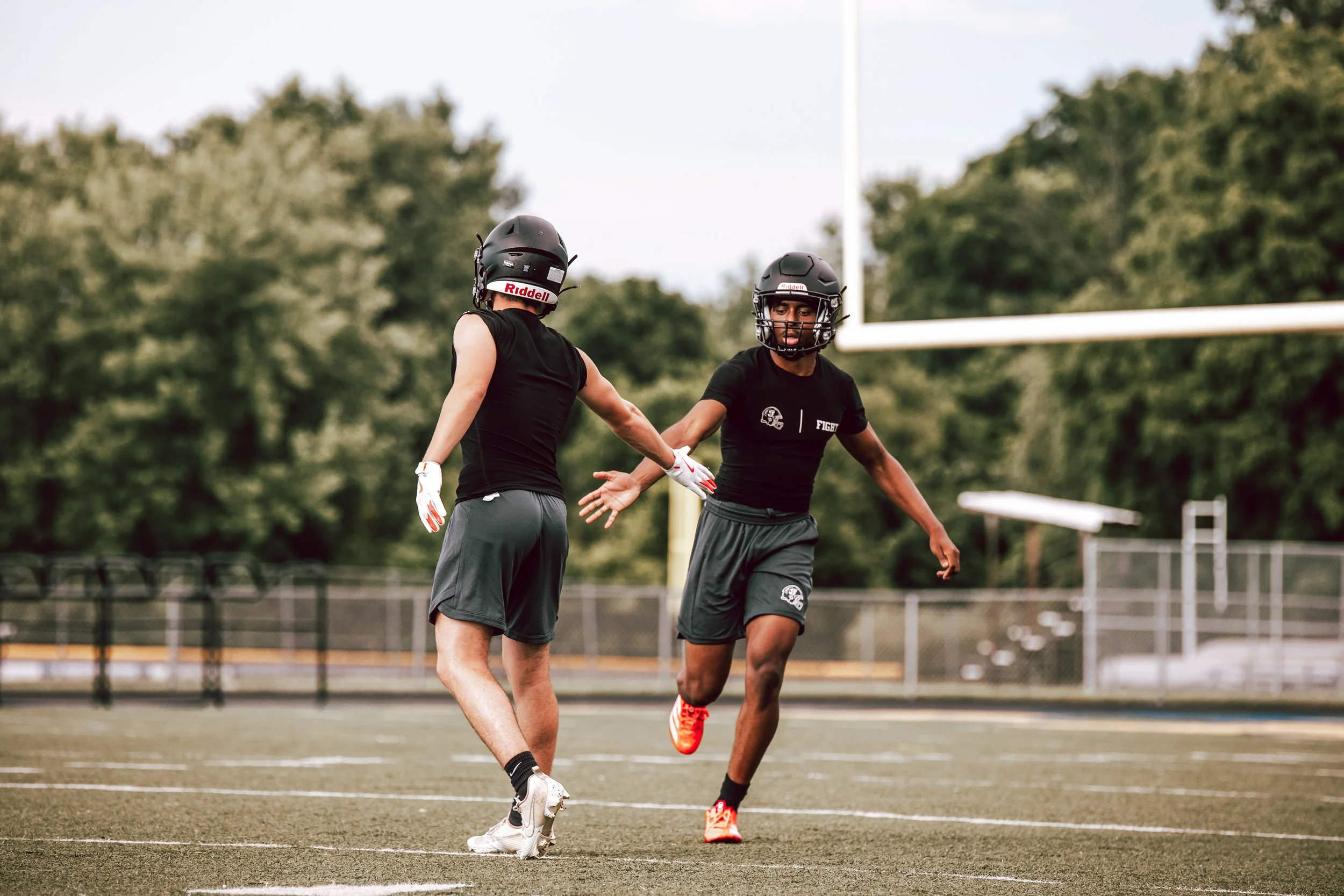 Two football players in black uniforms and helmets are on a football field, holding hands and celebrating.