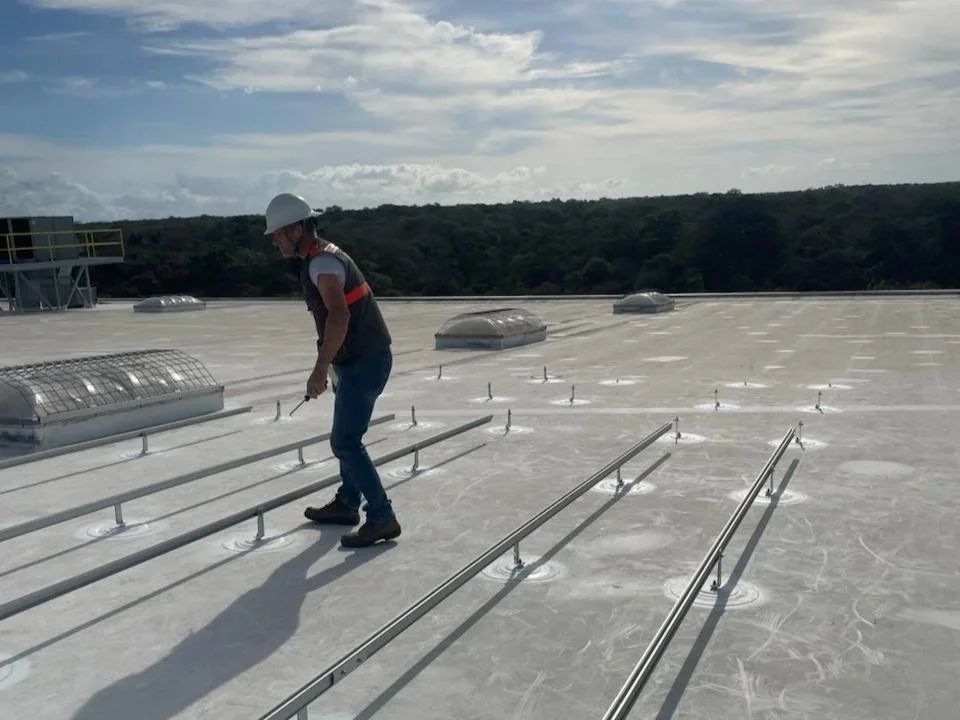 Persona con casco de seguridad inspeccionando un techo fotovoltaico con paneles solares sobre una estructura metálica instalada en membrana TPO en la zona de gauanacaste.