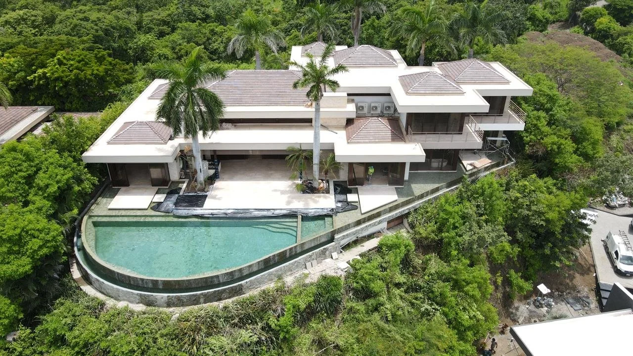 Casa moderna en colina con piscina y muchas palmeras rodeada de vegetación. Techo TPO instalado