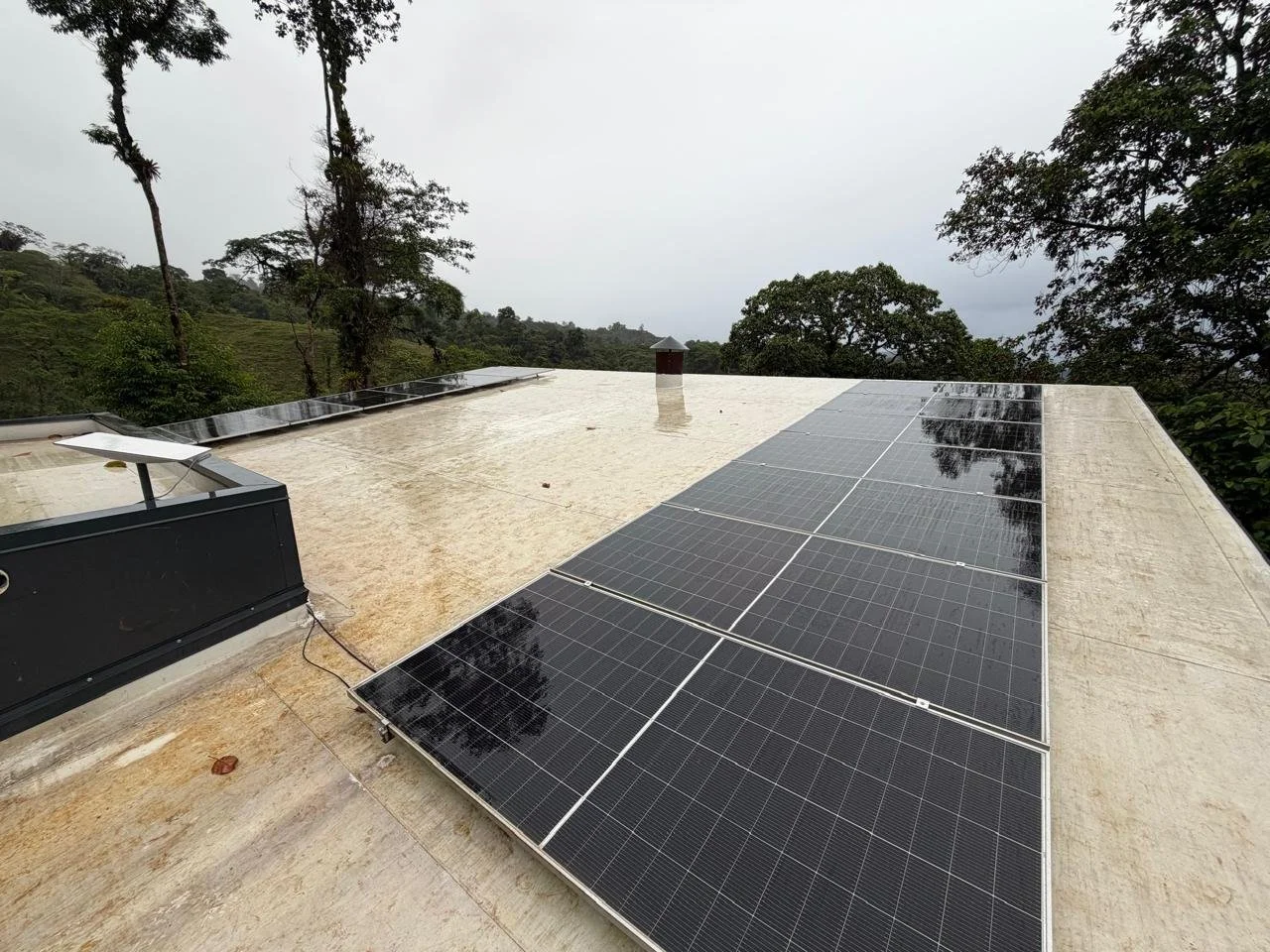 Paneles solares instalados en un techo TPO en zona lluviosa, con un fondo de árboles y cielo nublado. 