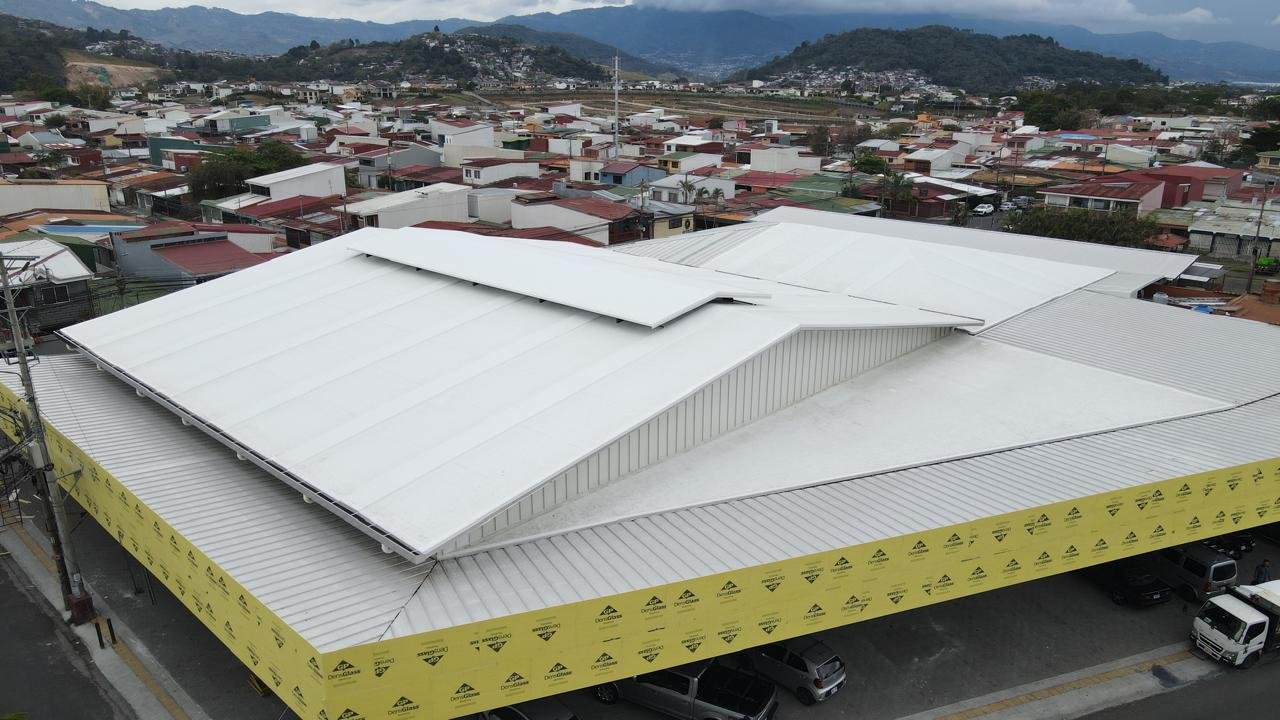 Techo de una tienda o edificio con techos de lámina metálica, cubierto con TPO y aislante termico en un área urbana con casas y colinas en el fondo