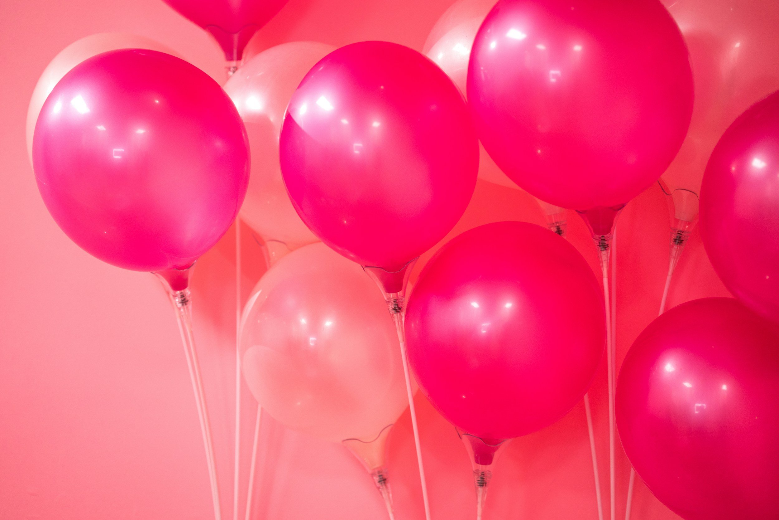A collection of pink and red balloons against a pink background.