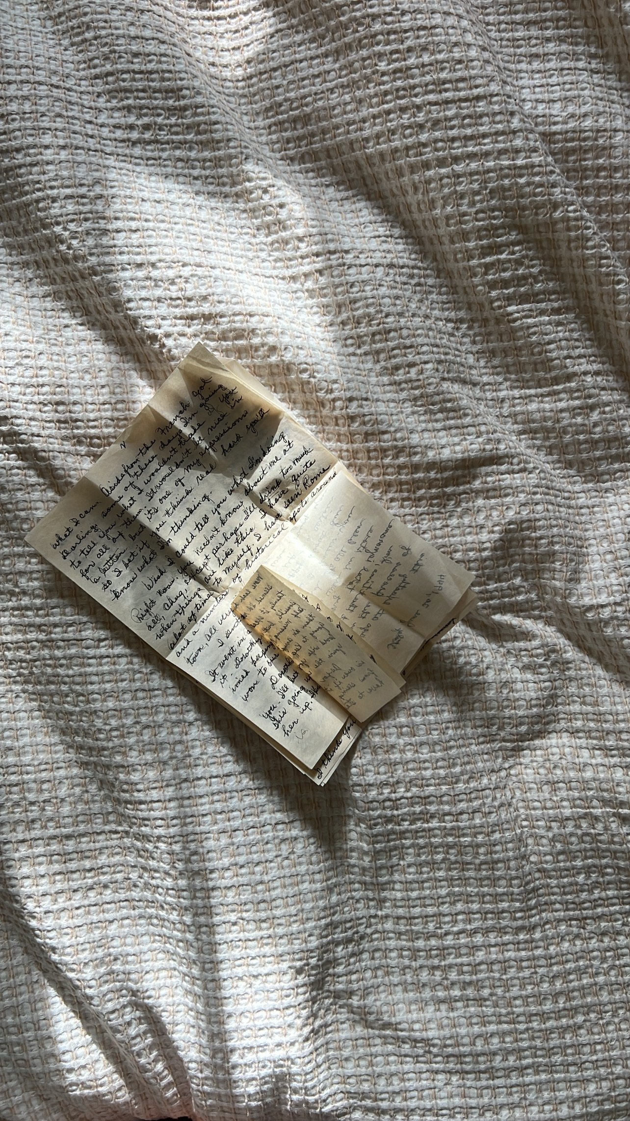 A handwritten letter on yellowed paper resting on a textured white fabric surface with a pattern of small squares.