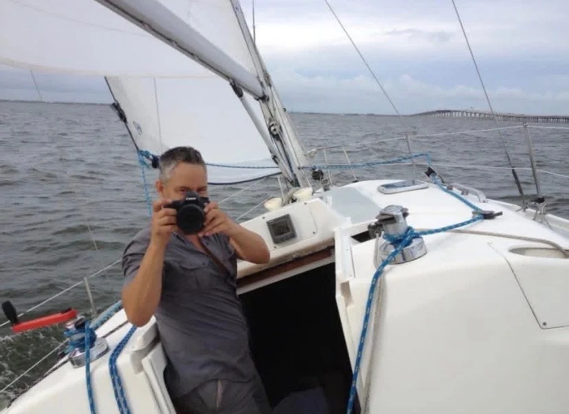 Person taking a photograph with a camera on a sailboat during a cloudy day.