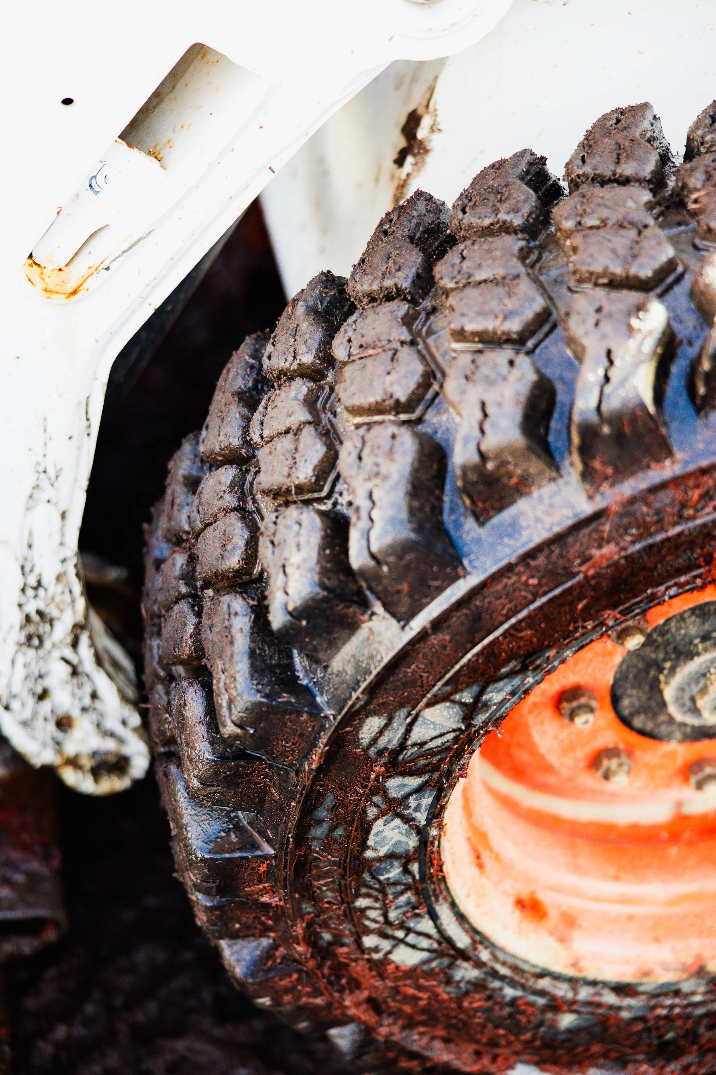 Close-up of a muddy off-road tire tread with an orange rim, on a vehicle with a white painted frame that has rust spots.