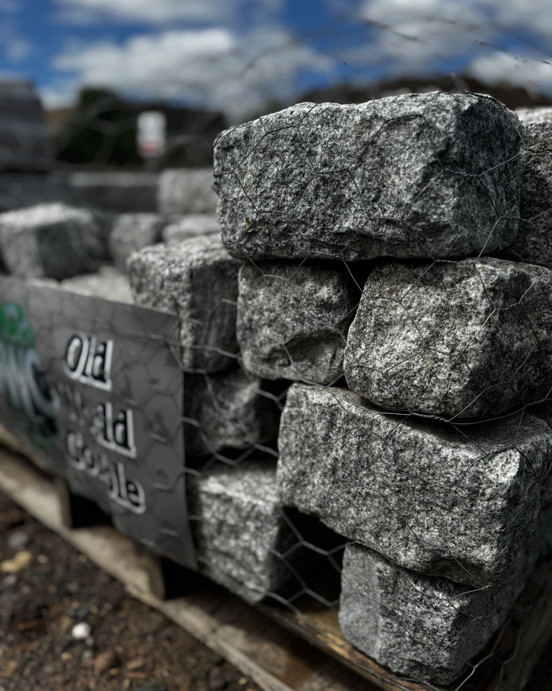 Stacked gray cobblestones wrapped with wire, placed on a wooden pallet on dirt ground.