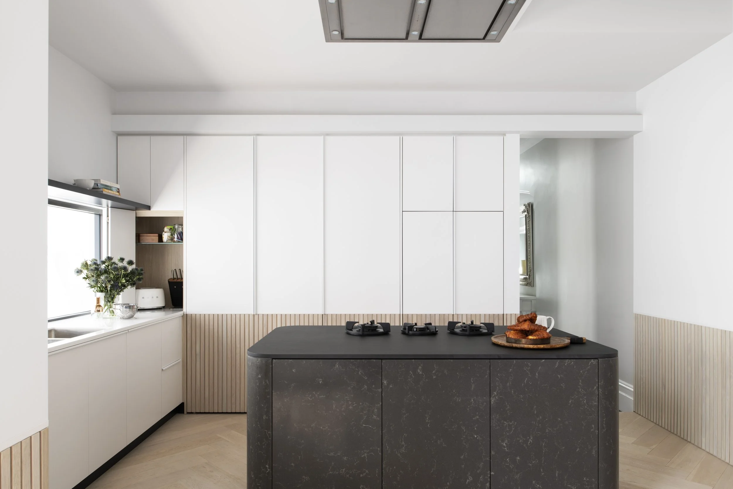 Modern kitchen with black island, white cabinets, wooden accents, and a window with plants.