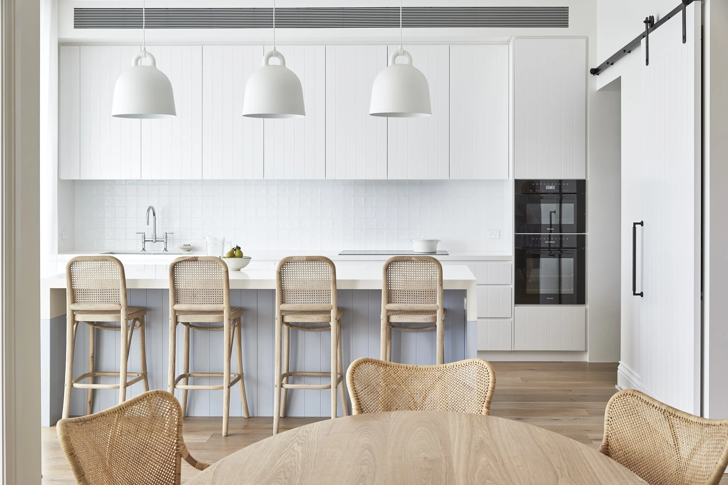 Modern white kitchen with bar seating, pendant lights, built-in oven, sliding barn door, and natural wood accents.
