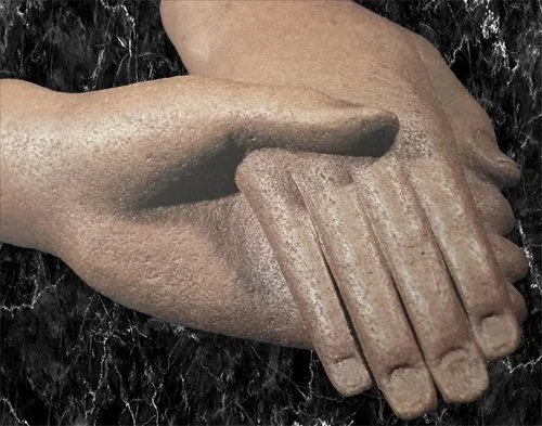 Close-up of a sculpture of two hands clasped together, one in front of the other.