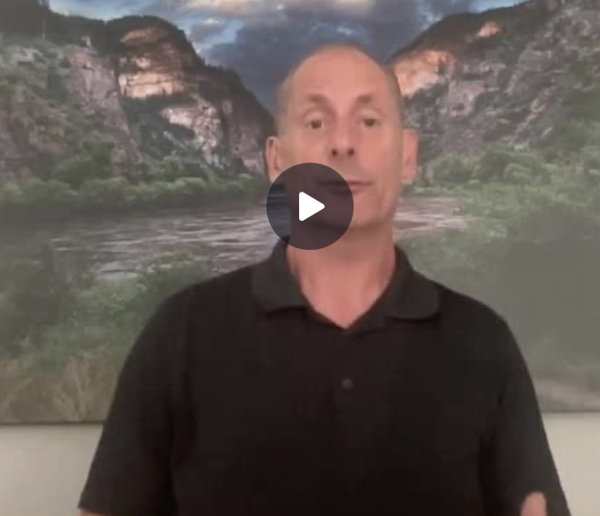 A man with short hair wearing a black polo shirt stands in front of a large scenic photograph of a river flowing through a mountainous landscape with trees and rocky cliffs.