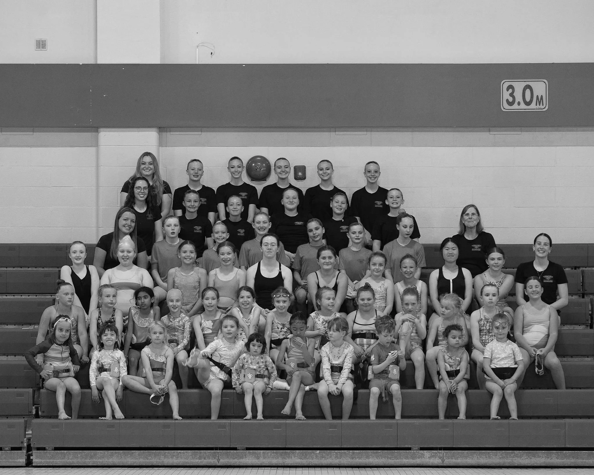 All club athletes and coaches posing for a photo, standing on bleachers, some wearing club uniforms.
