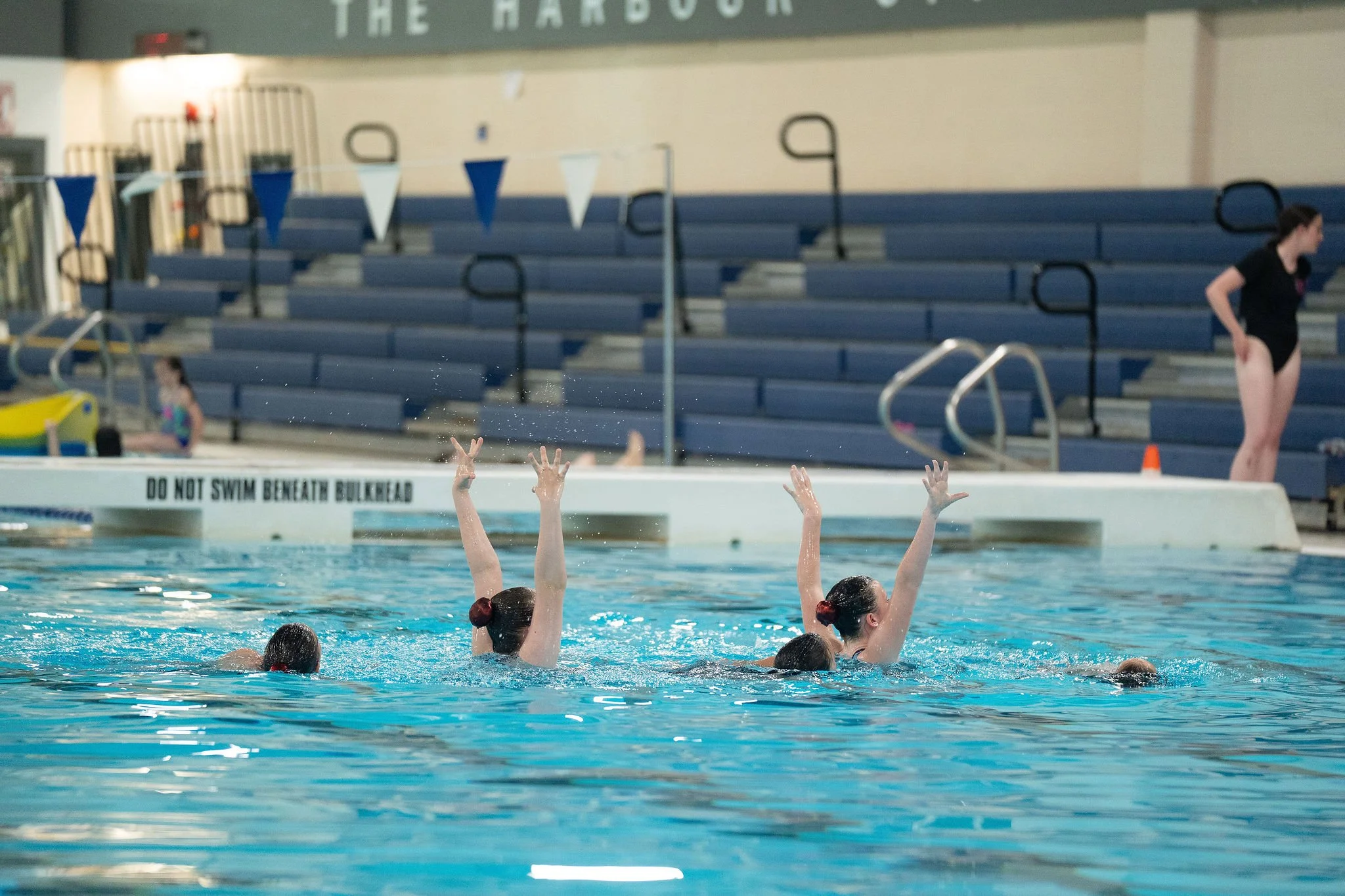 Young athletes performing in the pool, with bleachers in the background.