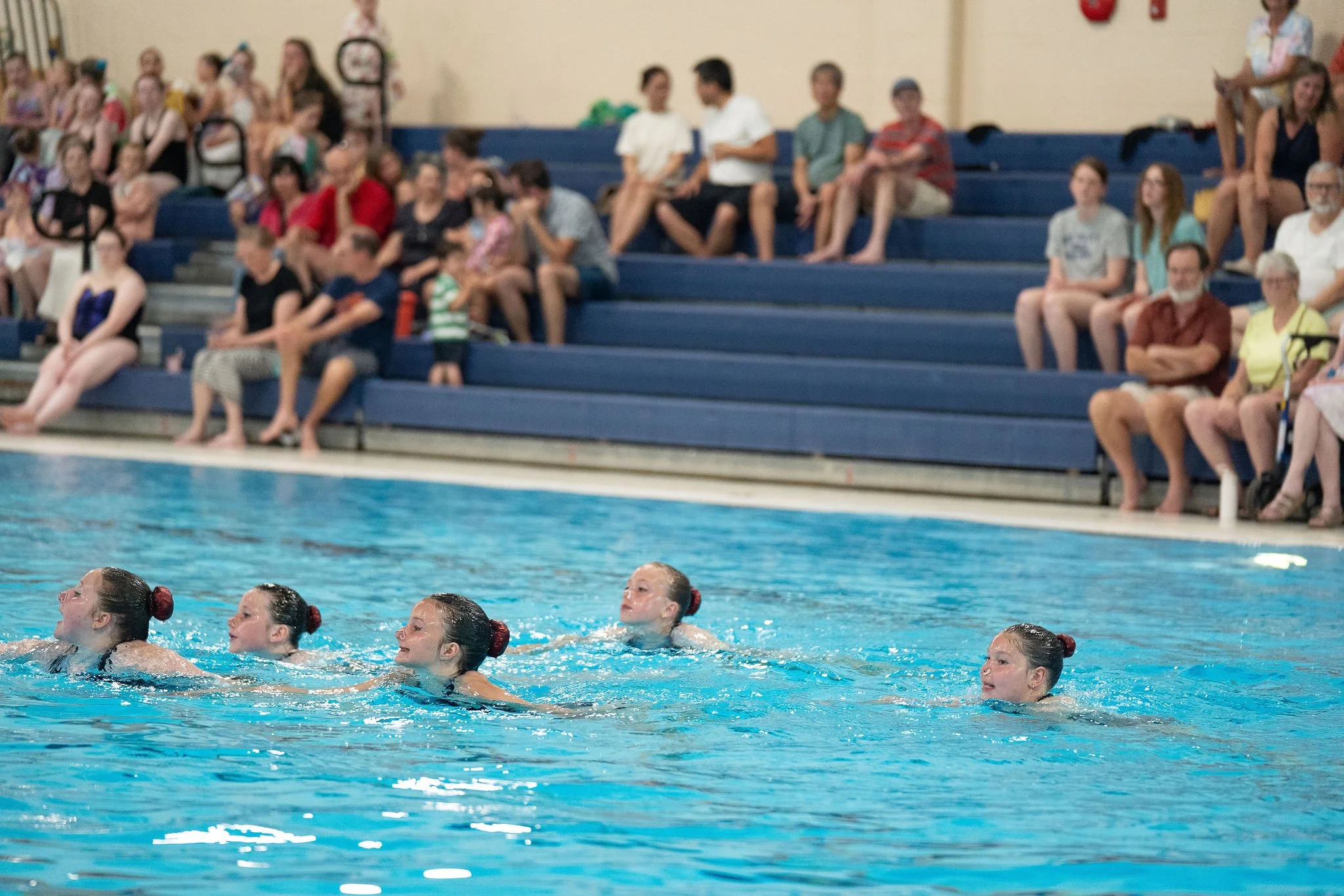 Young athletes performing in the pool, with bleachers in the background.