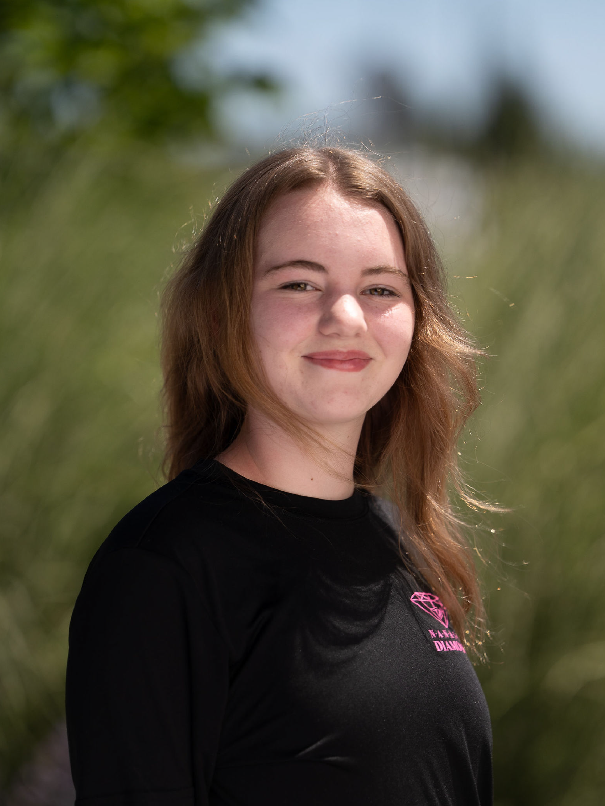 Coach Fiona, wearing a black shirt with pink nanaimo diamonds logo, standing in front of a brick wall.