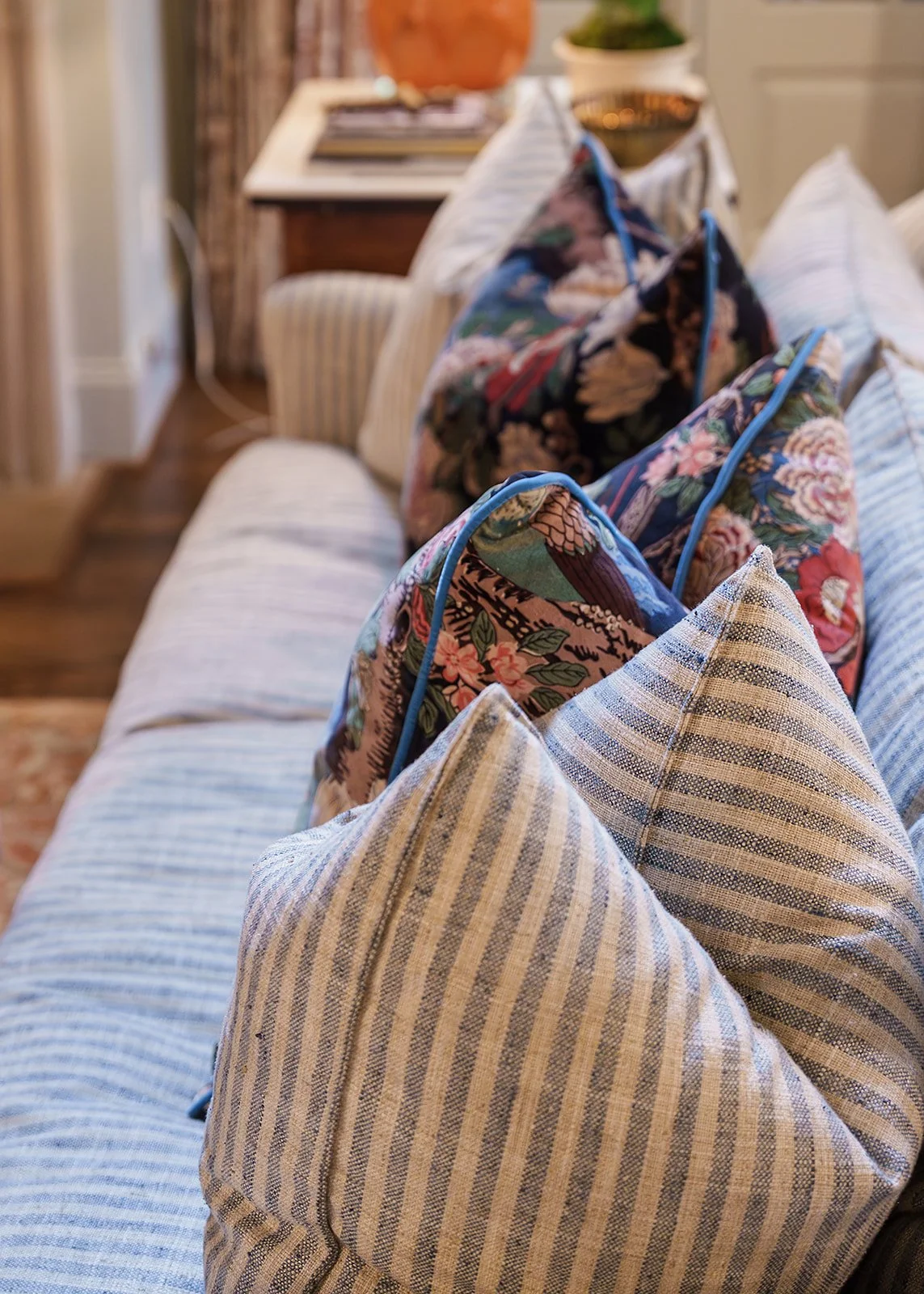 A row of pillows with blue and beige striped fabric and floral bags with floral patterns placed on a sofa.