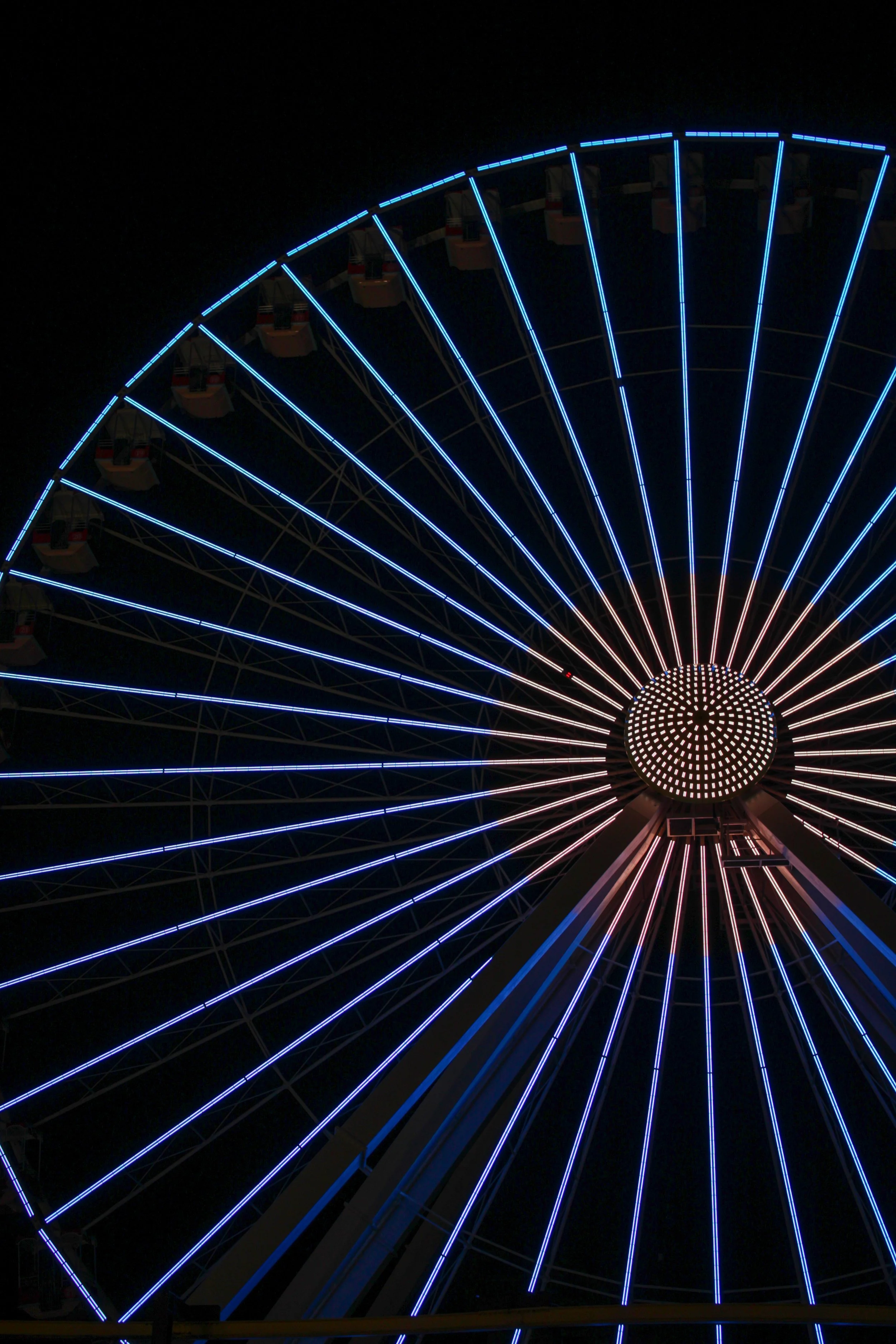 A brightly lit Ferris wheel at night with blue LED lights outlining its structure and a dark sky background.
