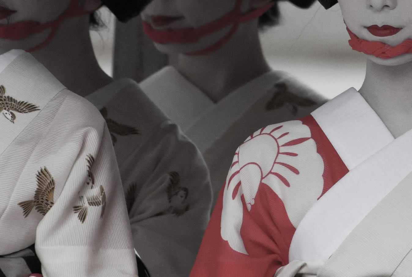 Three women wearing traditional Geisha attire with white face makeup, red lipstick, and kimonos with intricate patterns. They are looking down or away, with close-up focus on their faces and shoulders.