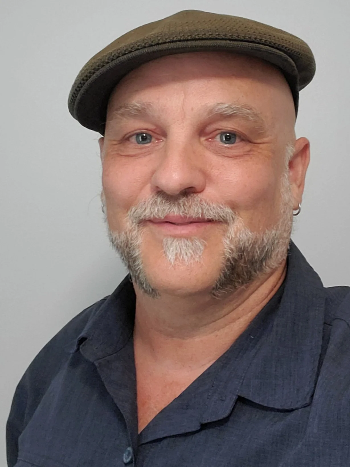 Portrait of a smiling man wearing a flat cap and dark collared shirt.
