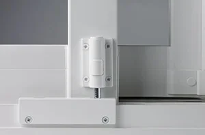 Close-up of a white door hinge mounted on a white door and frame, with gray wall in background.