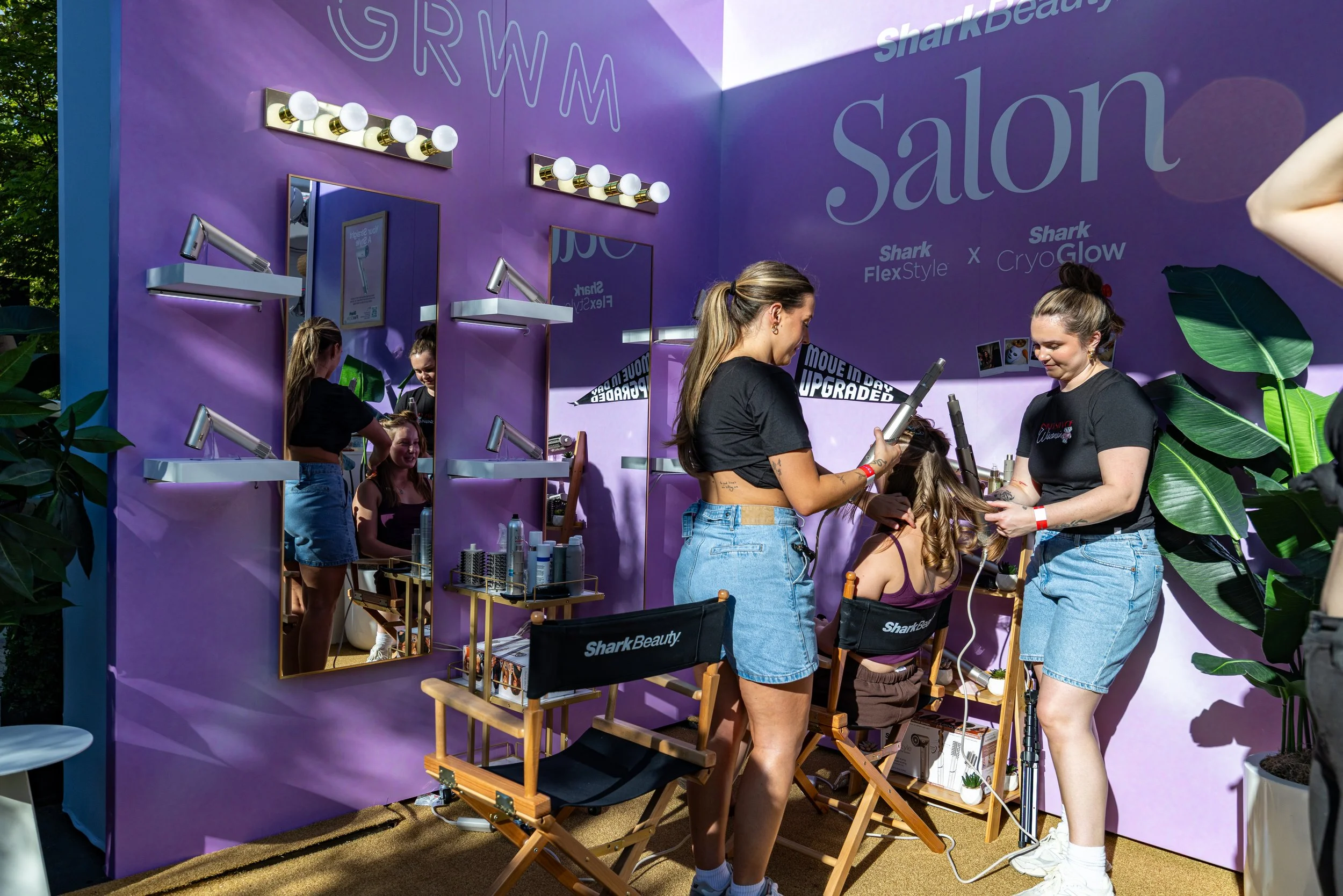 People getting beauty treatments at a Shark Beauty booth with mirrors, lights, and purple walls.