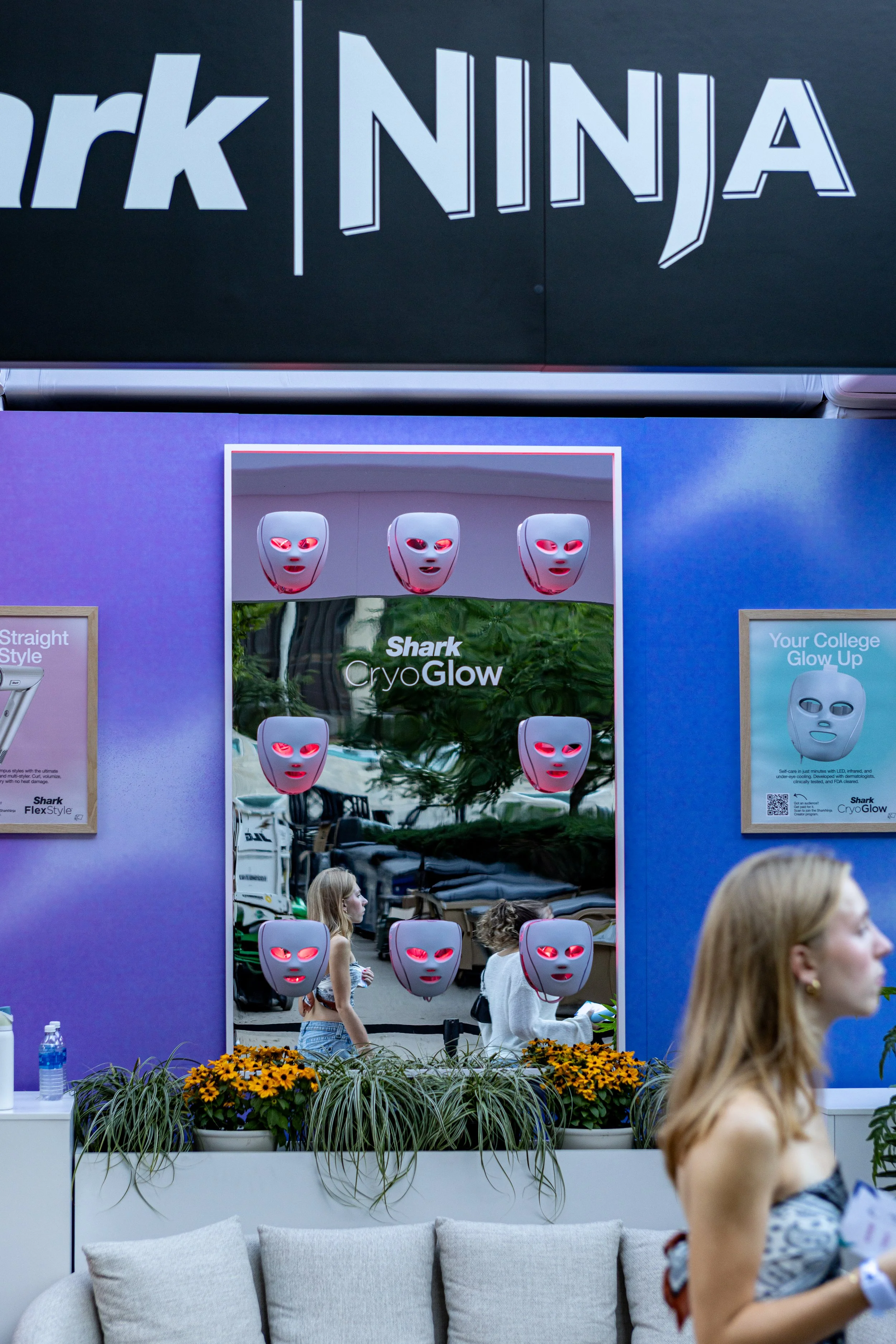 Trade show booth displaying Shark CryoGlow facial therapy masks, with people walking and talking in the background.