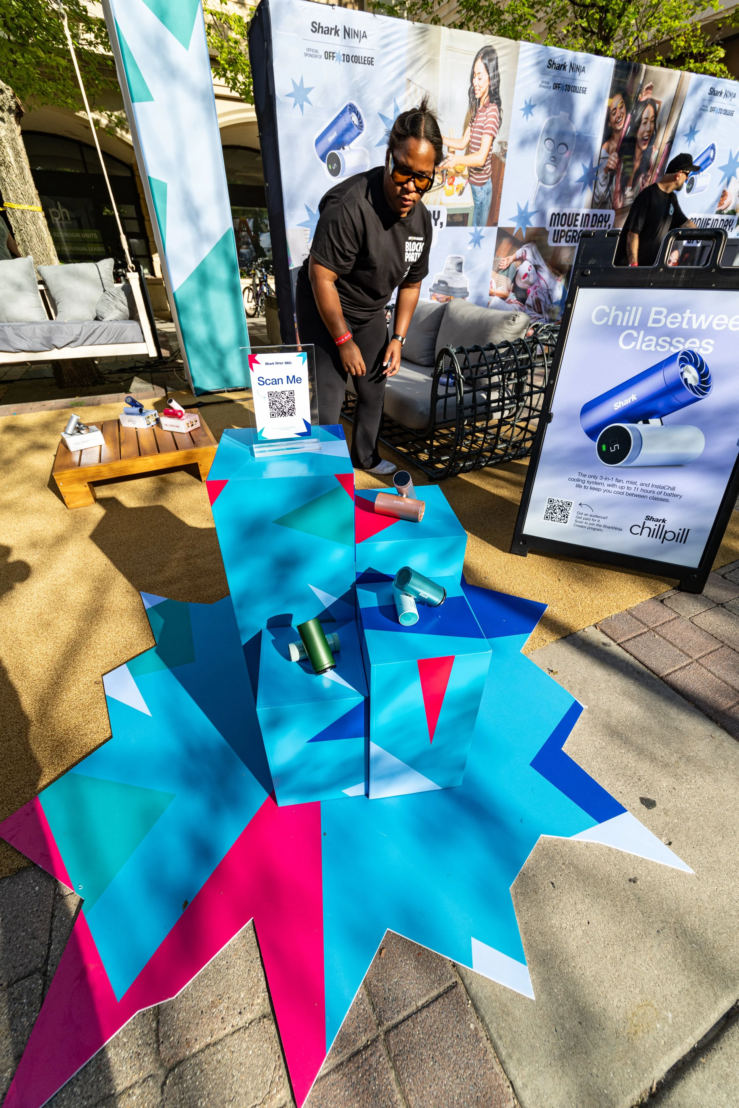 Outdoor display promoting Shark Ninja bladeless fans with colorful geometric shapes, signs reading "Scan Me" and "Chill Between Classes," and four portable bladeless fan devices in various colors.