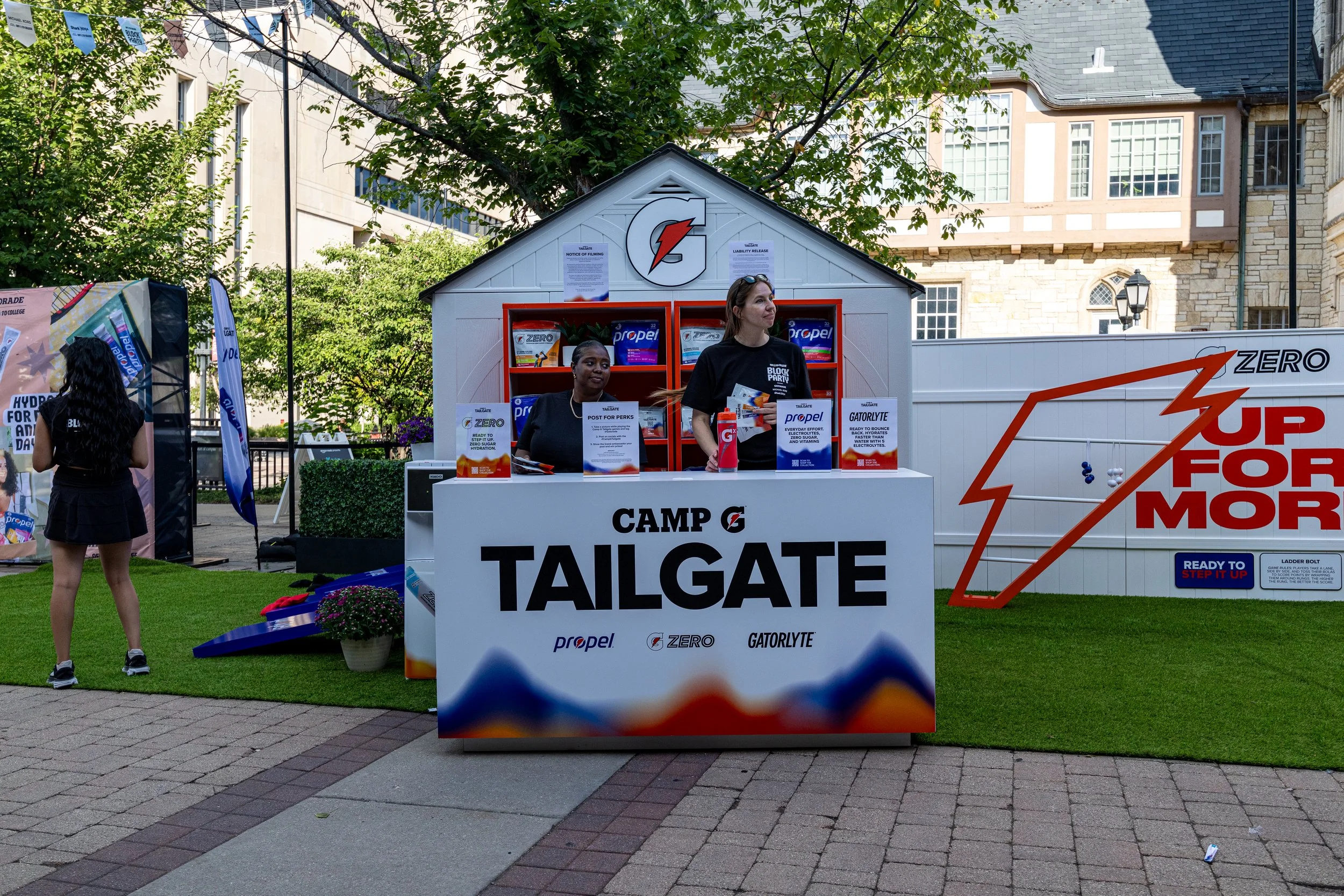 People at a Gatorade tailgate event with promotional displays and signs, set on a grassy outdoor area in front of historic buildings.